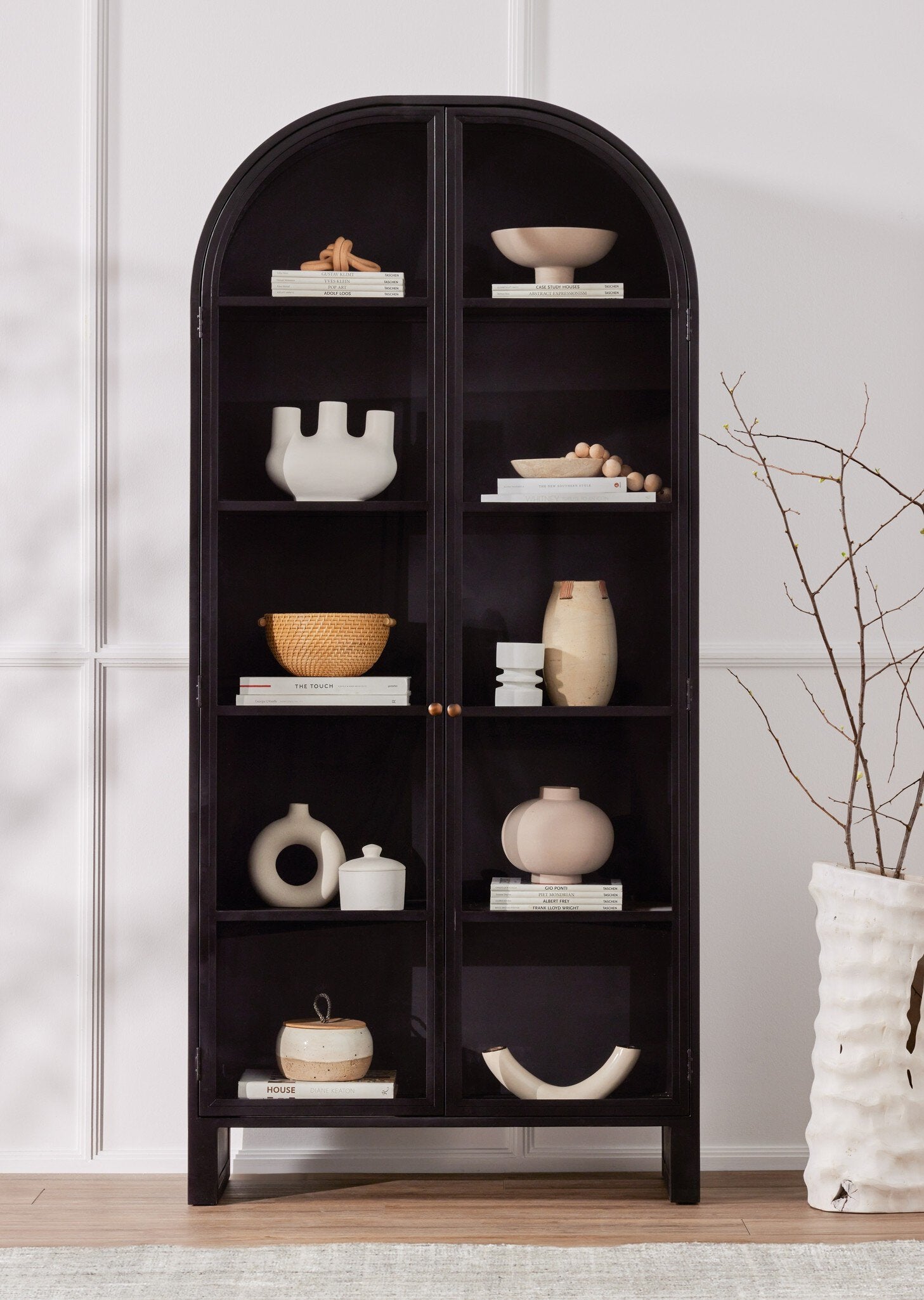 Black arched bookshelf with decorative items against a light gray wall.