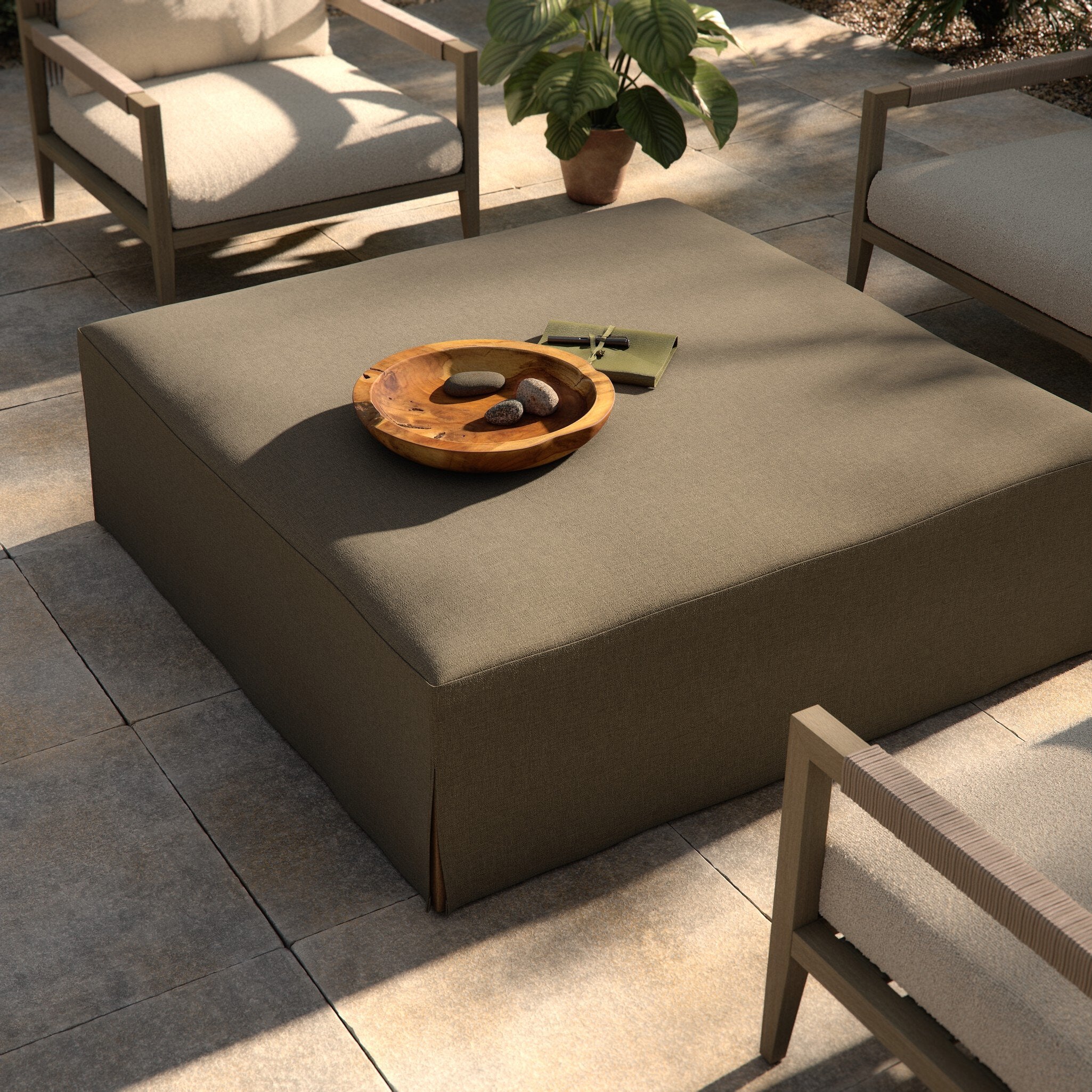 Outdoor patio setting with a square ottoman and decorative items on a stone patio.