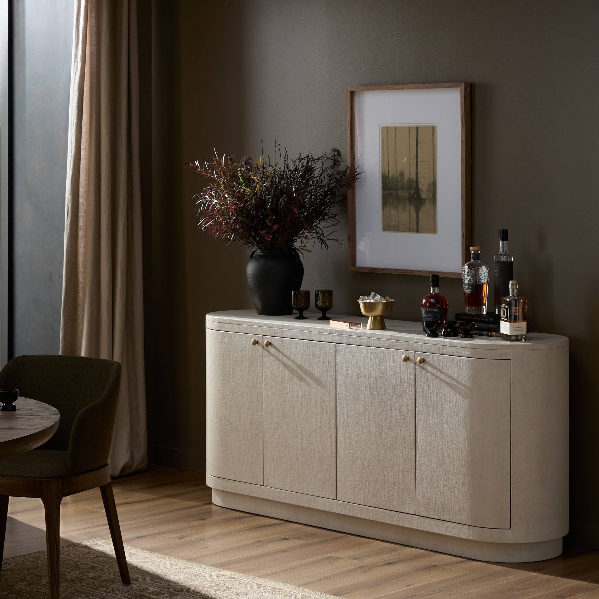 Ivory sideboard with decorative items in a room with a curtain and painting.
