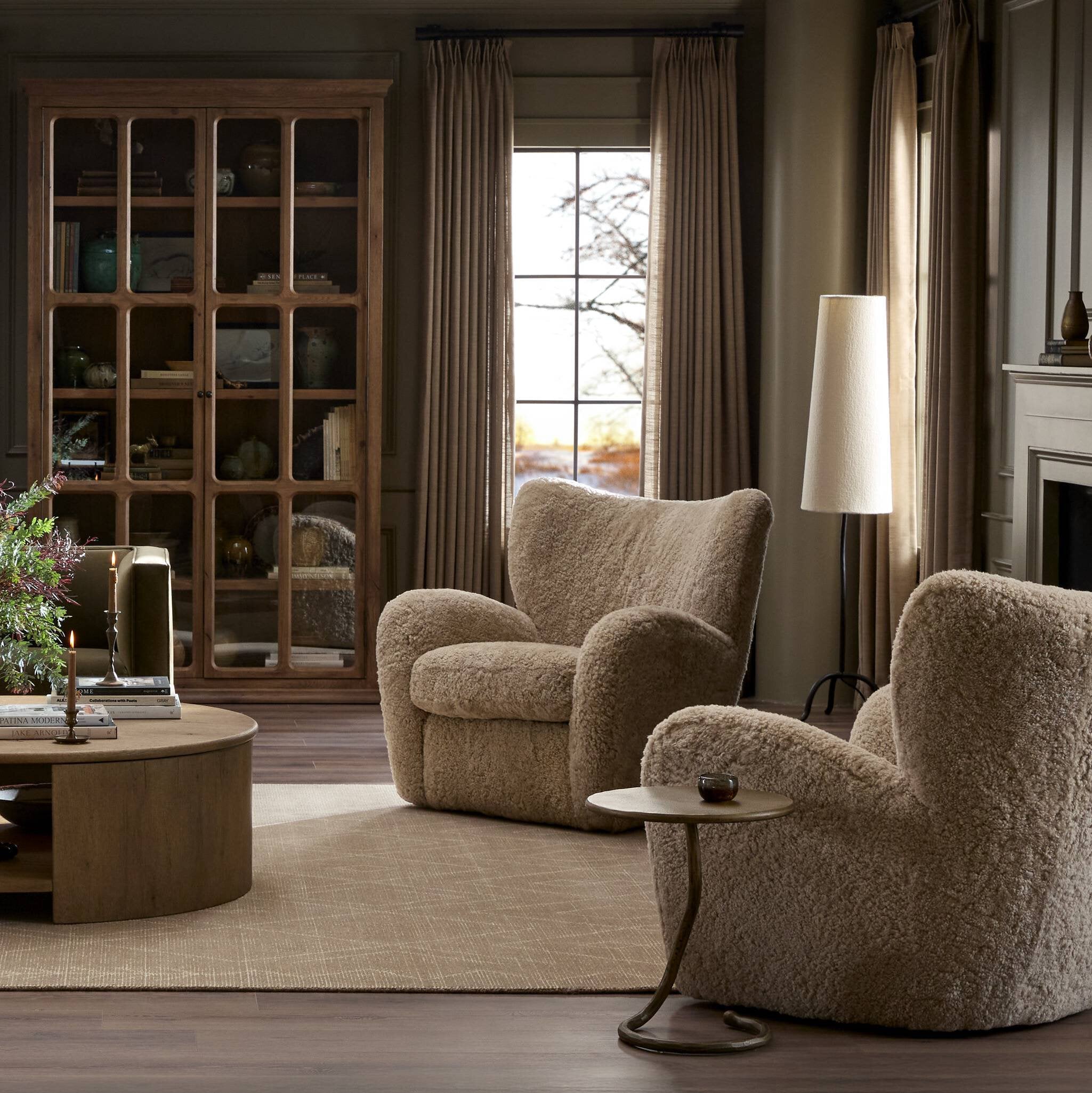 Cozy living room with two beige armchairs, a round wooden table, and a bookshelf.