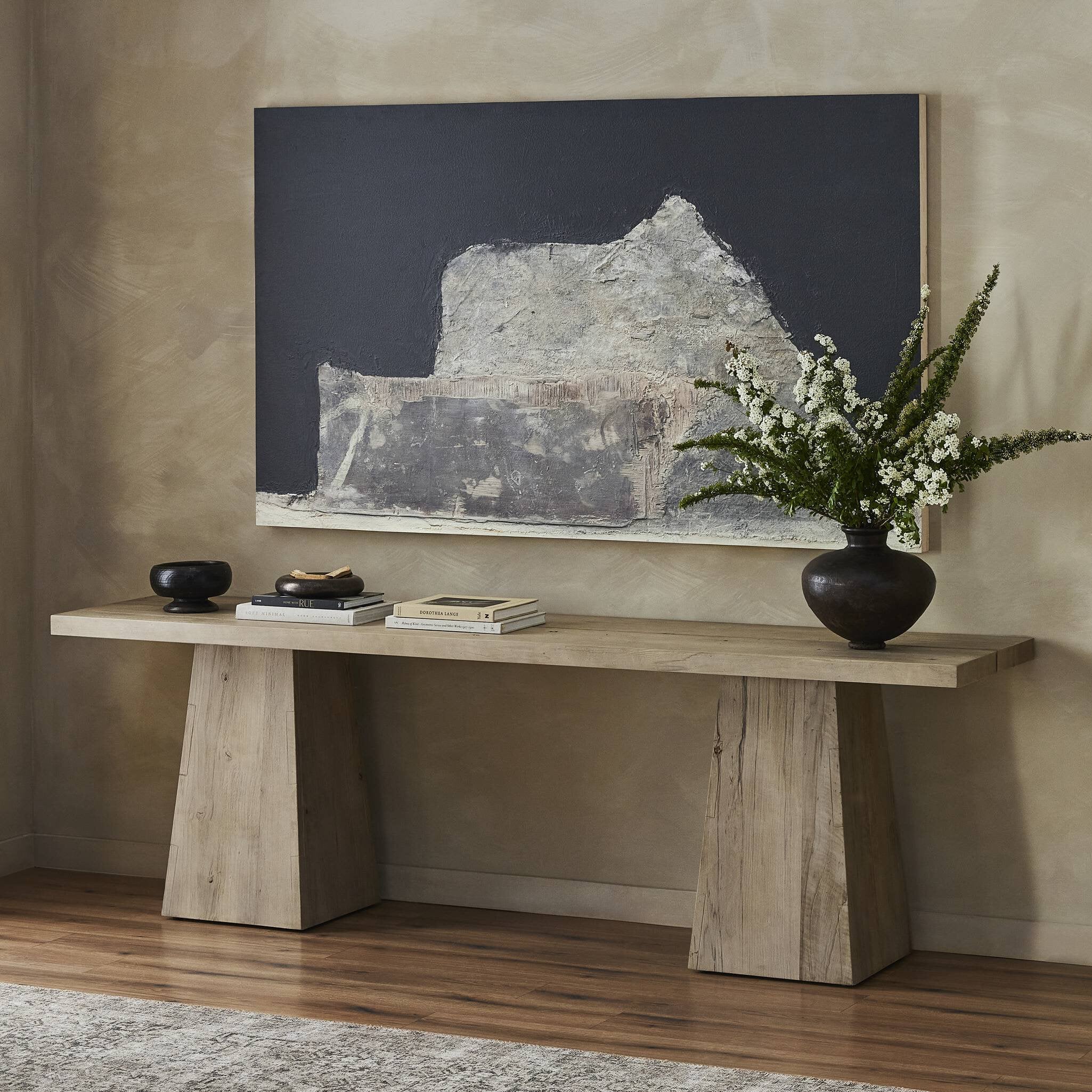 Wooden console table with decorative items against a wall with a large abstract painting.