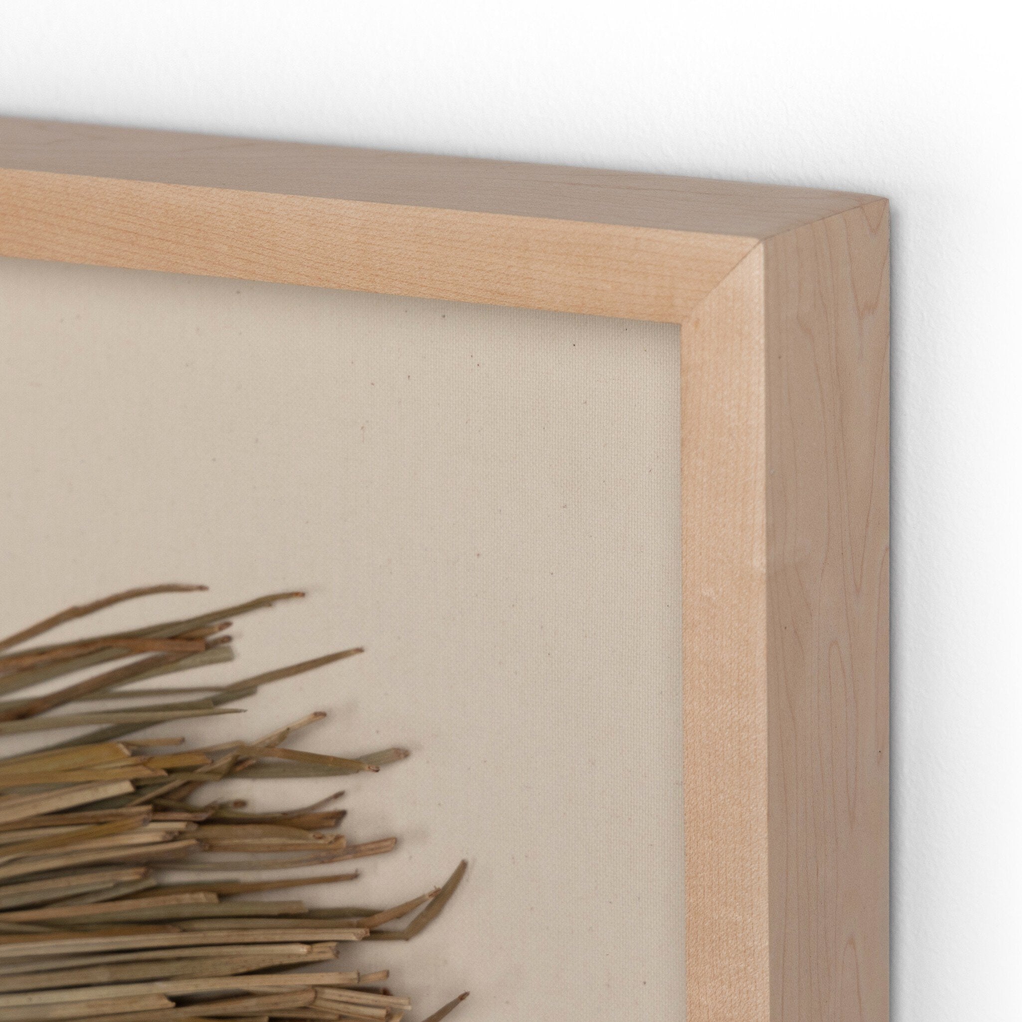 Close up of the framed palm leaf decorative wall art with a circular, fan-like design on a beige background.