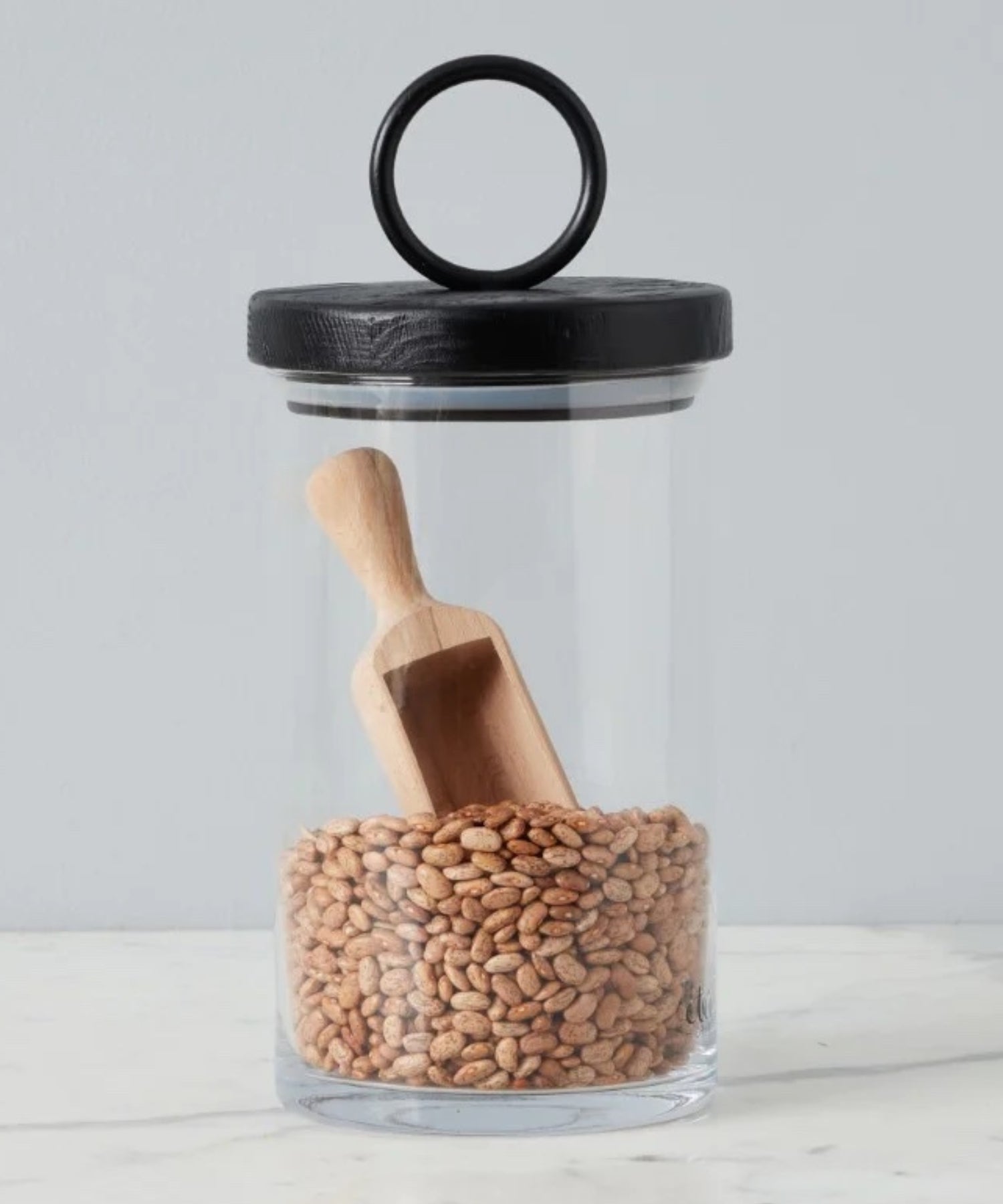 Beechwood scoop with a short handle and a broad, shallow bowl styled in a glass canister with black lid.