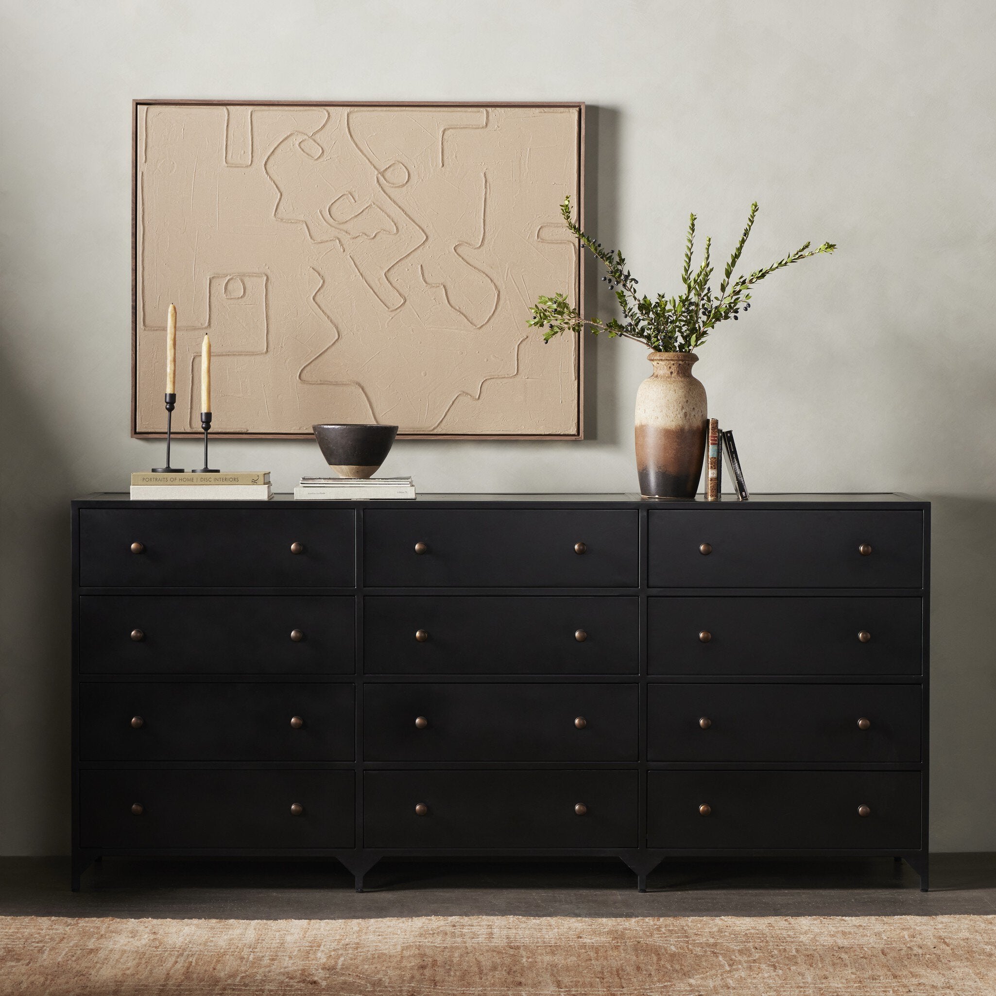 Black dresser with decorative items including a map, candles, and a vase against a neutral wall.
