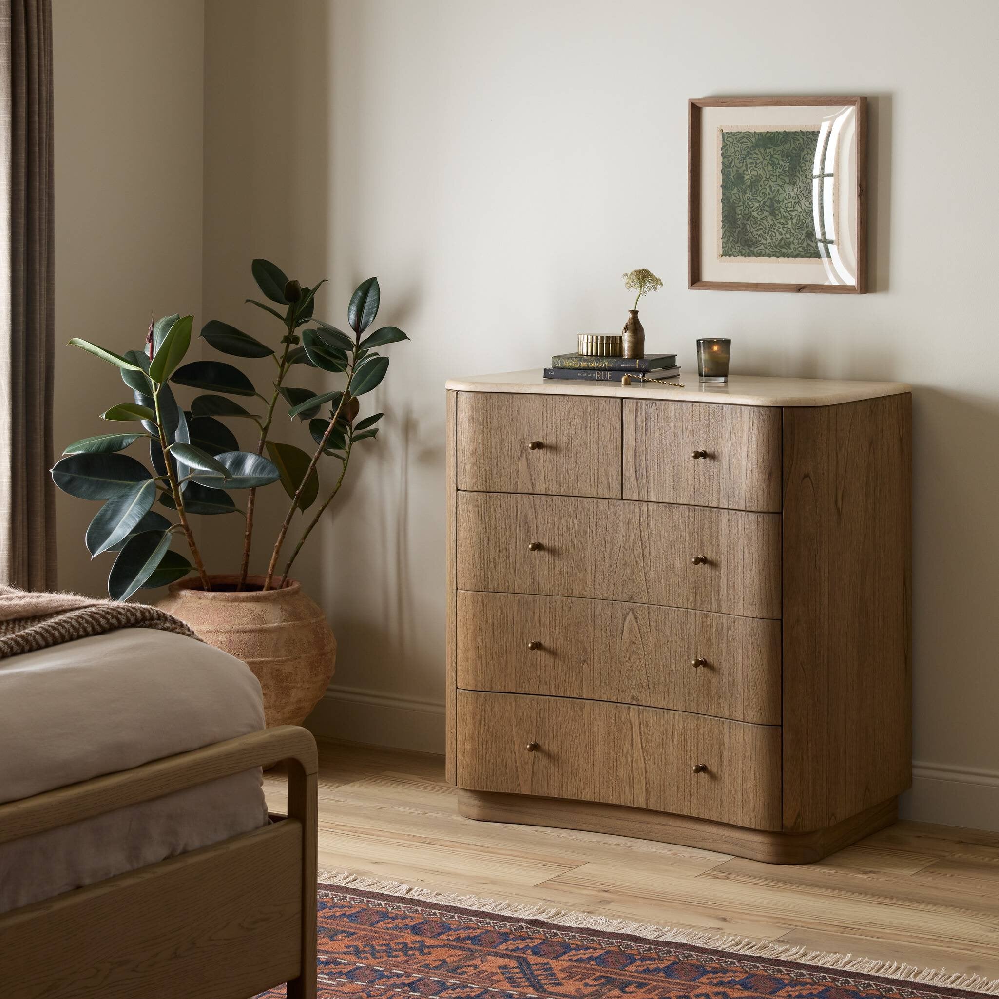 Wooden dresser in a bedroom with a plant and framed picture on top