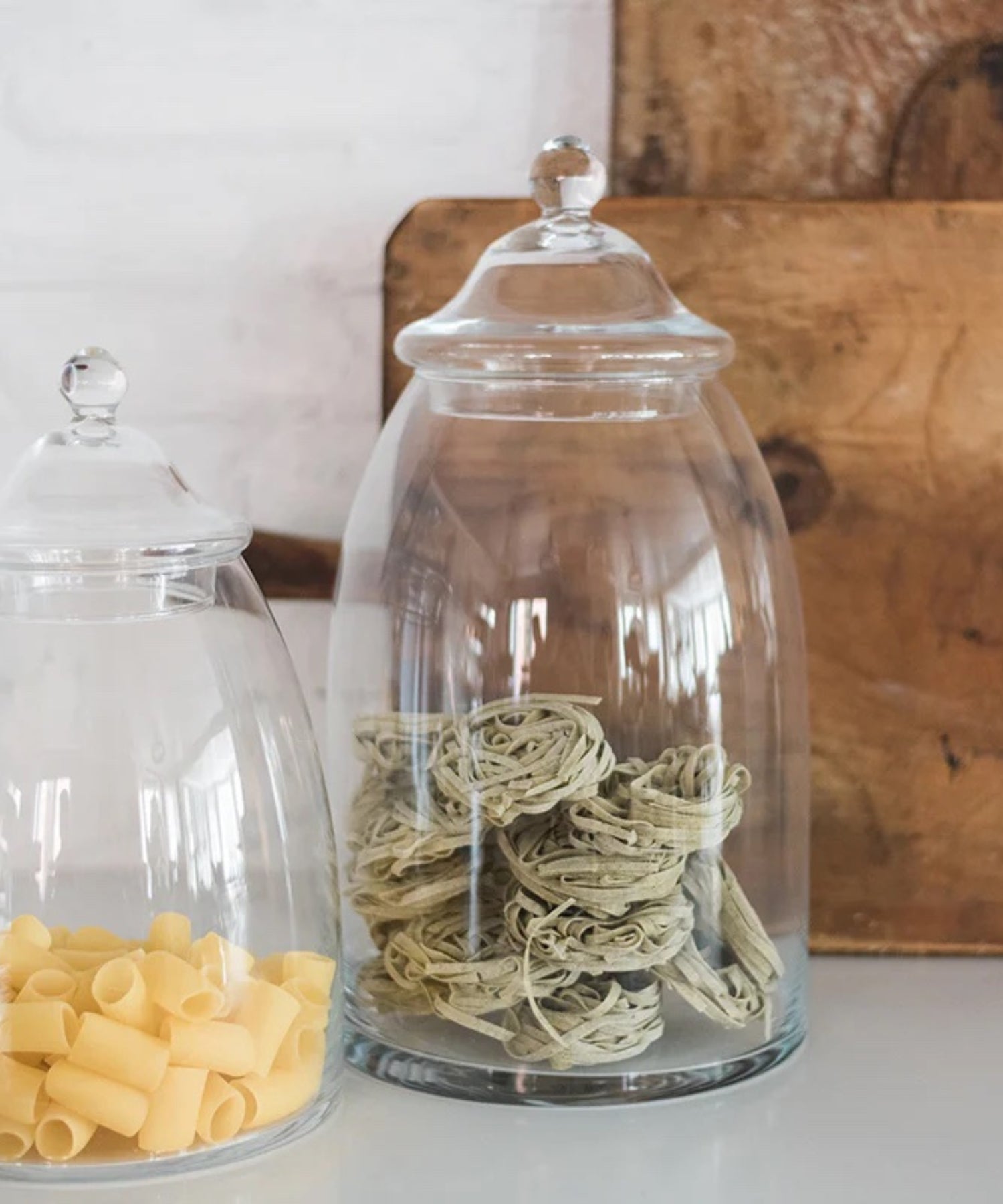 Two clear glass apothecary jars with a domed lid and rounded knob. Each styled with pasta.