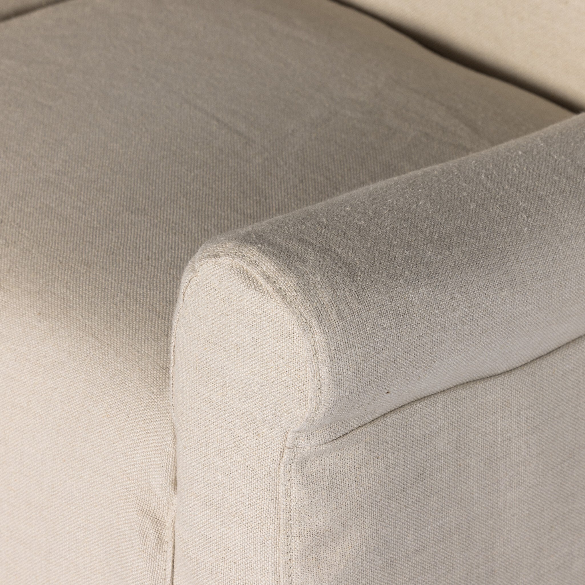 Close up of a natural slipcovered dining armchair detailing its fabric texture and rolled arms.
