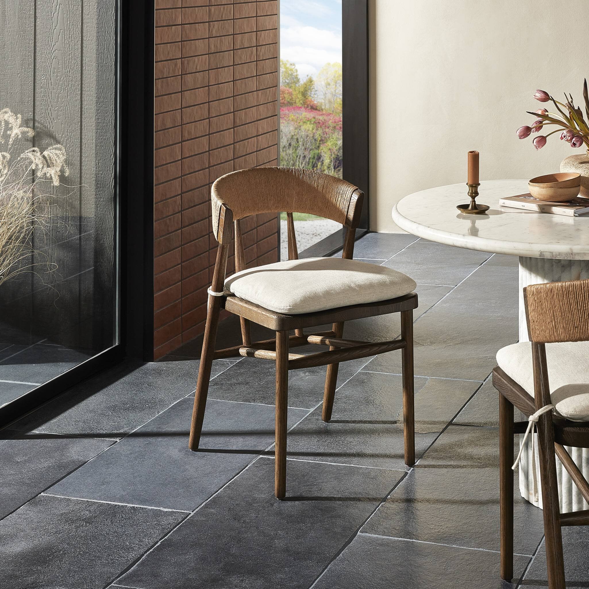 Wooden chair with a cushion on a stone patio next to a dining table.