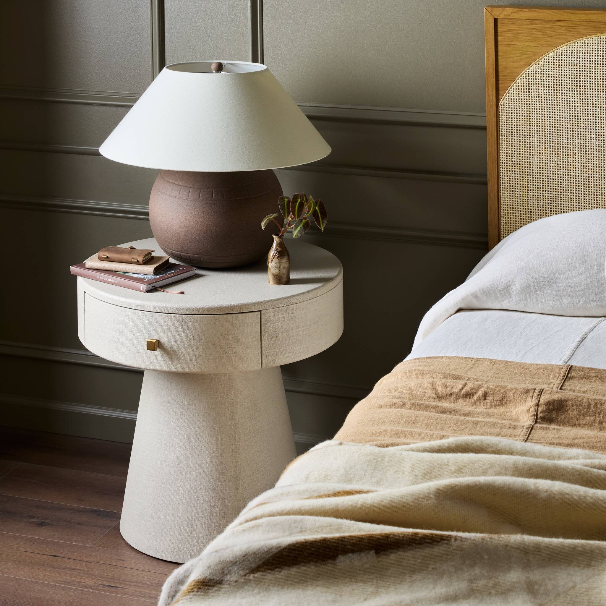White nightstand with a lamp next to a bed with beige bedding.