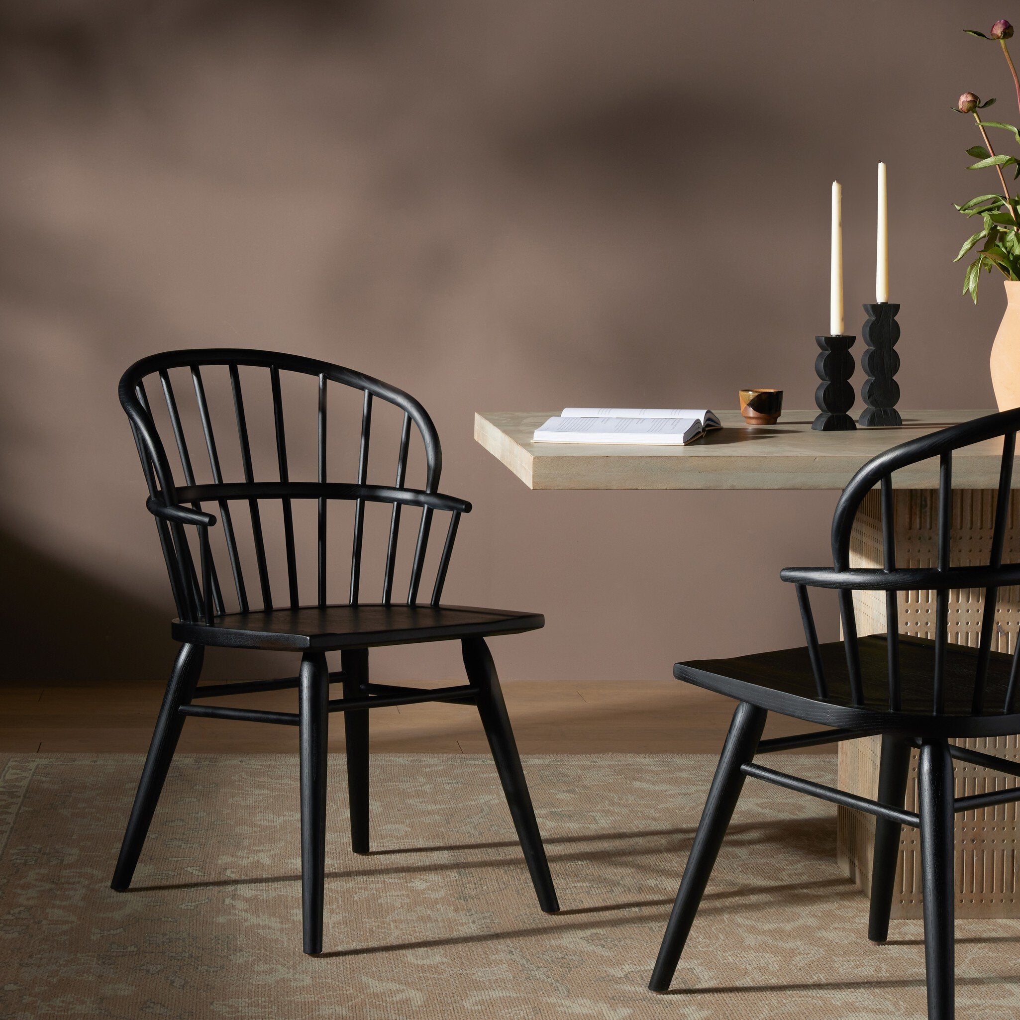 Two black dining chairs in a room with a dining table and candles.