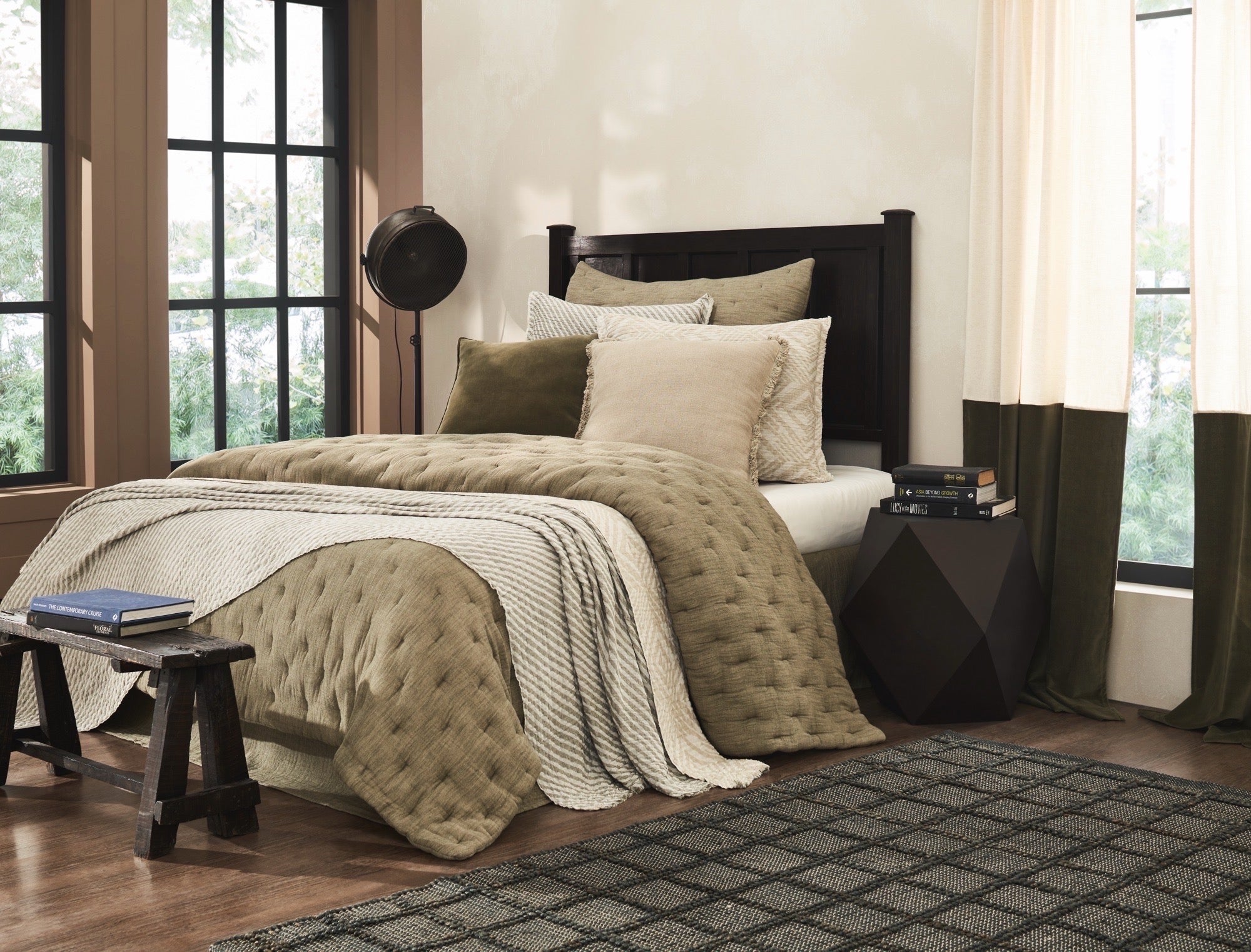 Bedroom with a bed featuring green and beige bedding, a wooden bench, and large windows.