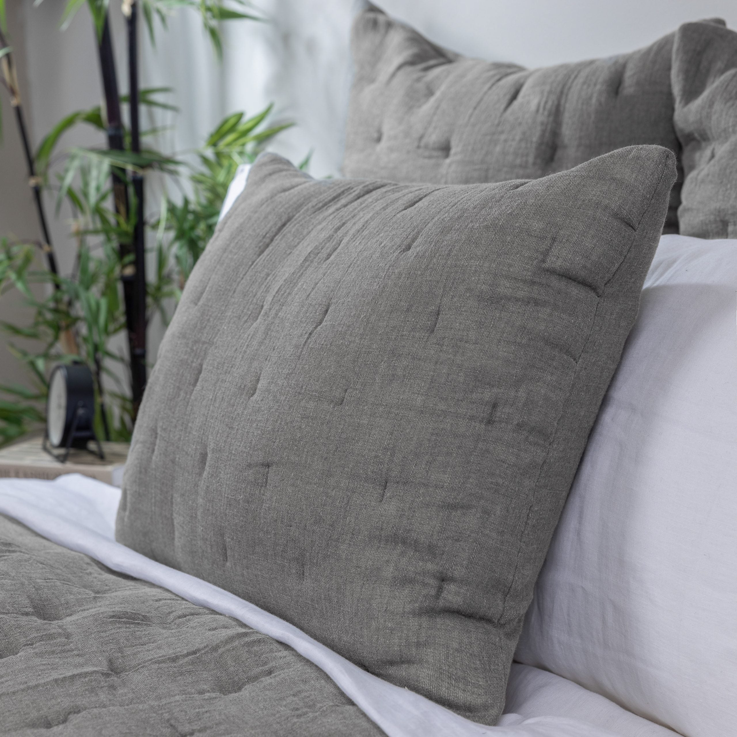 Styled bed with gray textured pillows and matching grey quilt with white sheets detailing material and texture.
