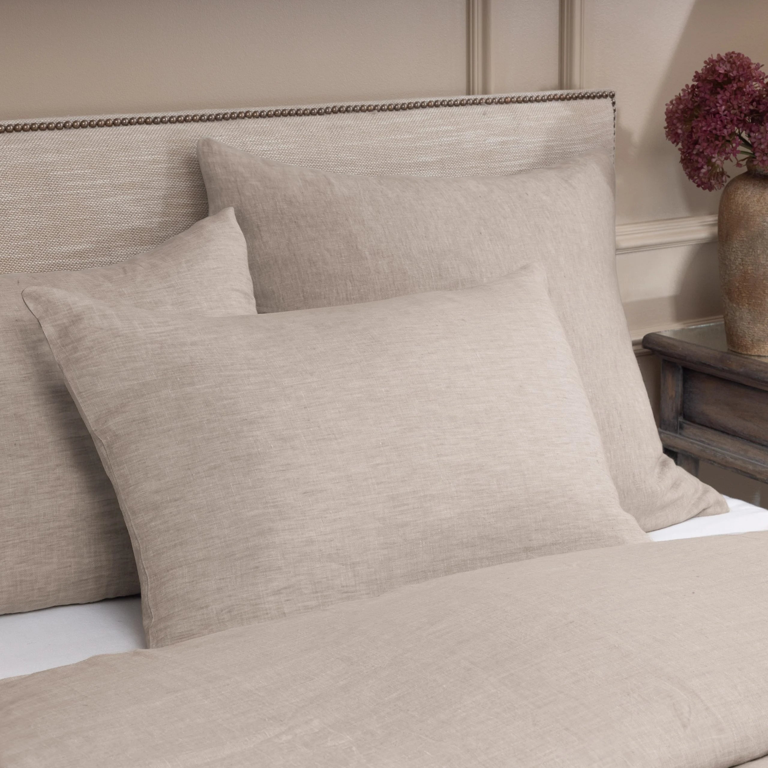 Beige textured pillows on a bed with a neutral headboard and side table.