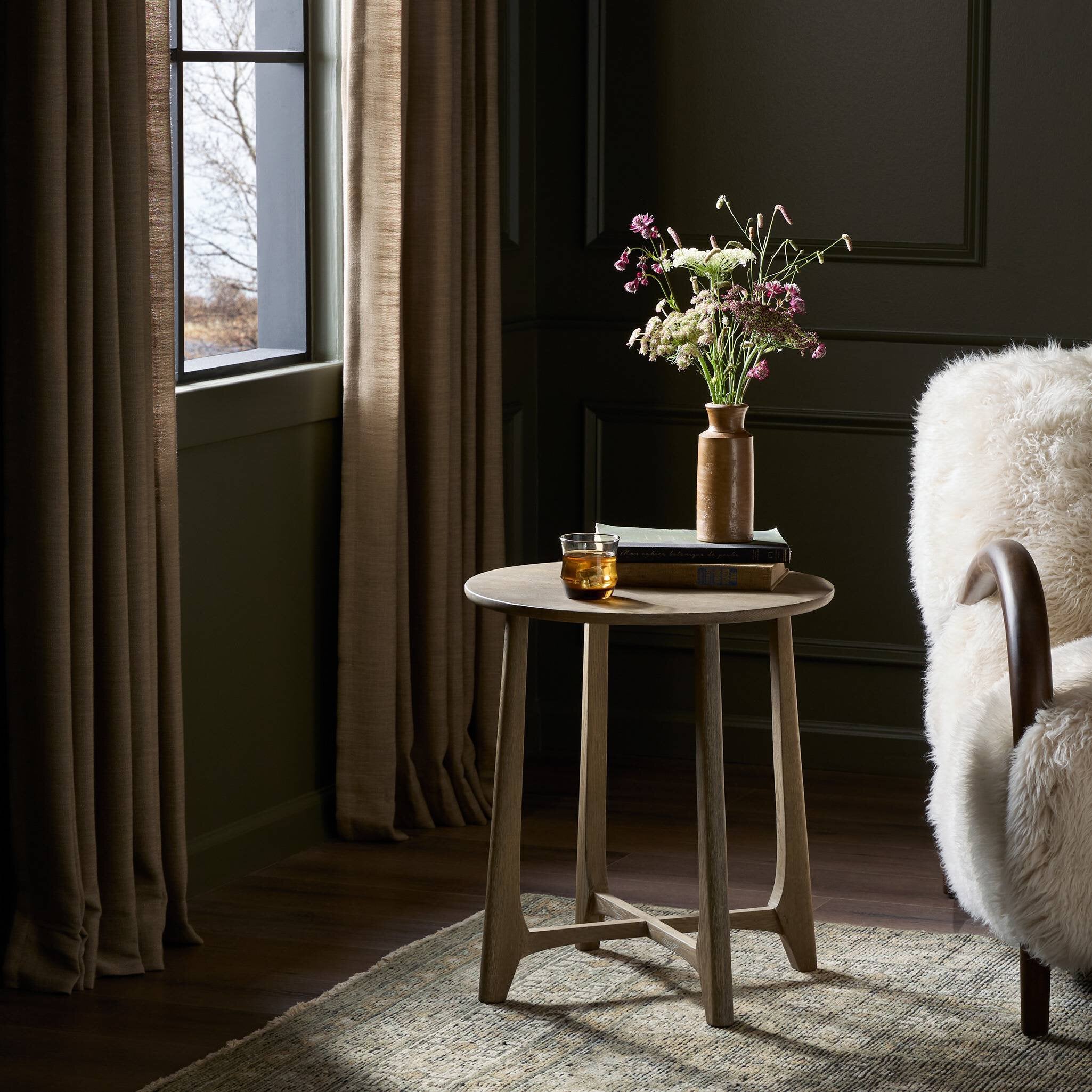 Small round wooden table with a vase of flowers and a glass in a dimly lit room.
