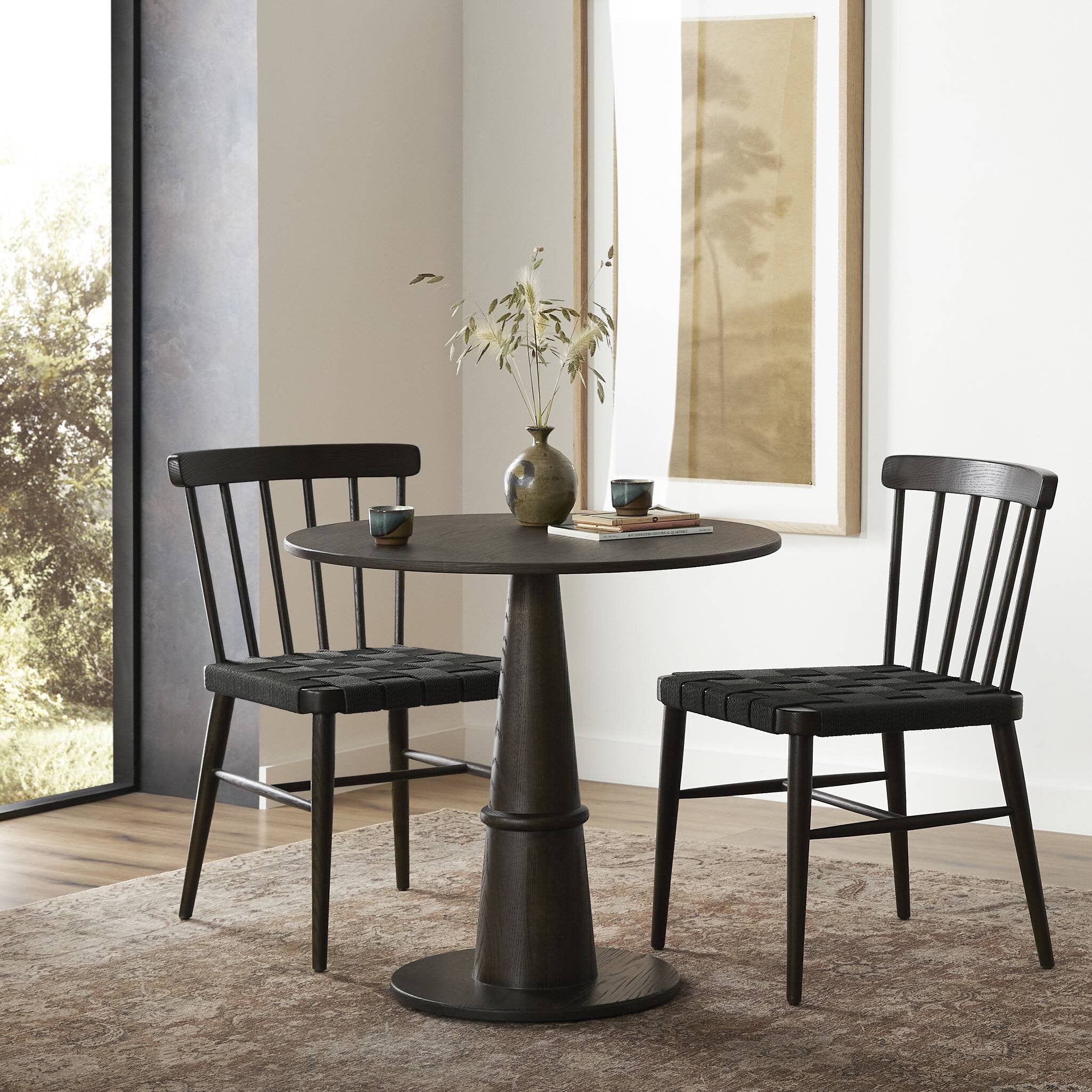Dining set with black round table and chairs in a room with large windows.