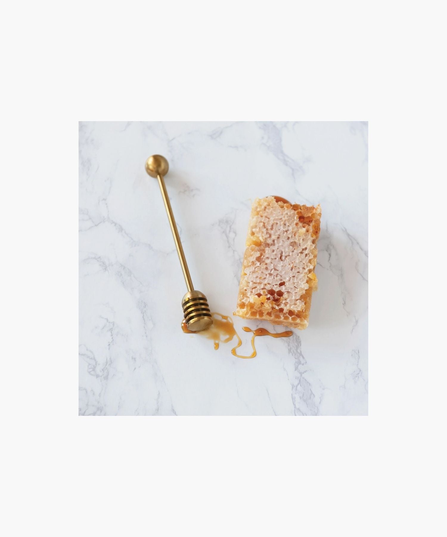 Gold honey dipper with a round handle and grooved end for collecting honey styled with honey comb on a marble surface. Simple and elegant kitchen tool.