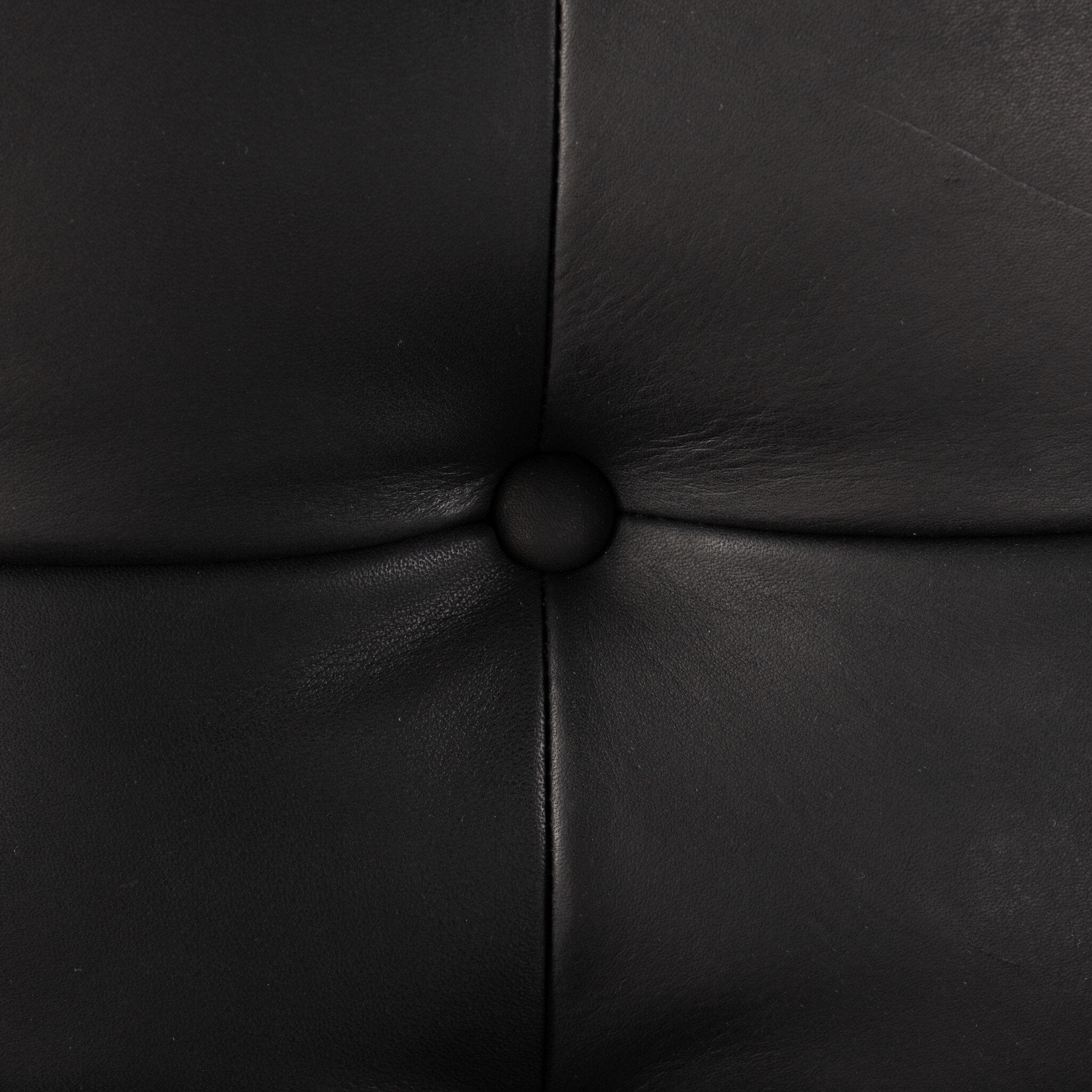 Close up of a tufted black leather sling style armchair with wooden frame on a white background.