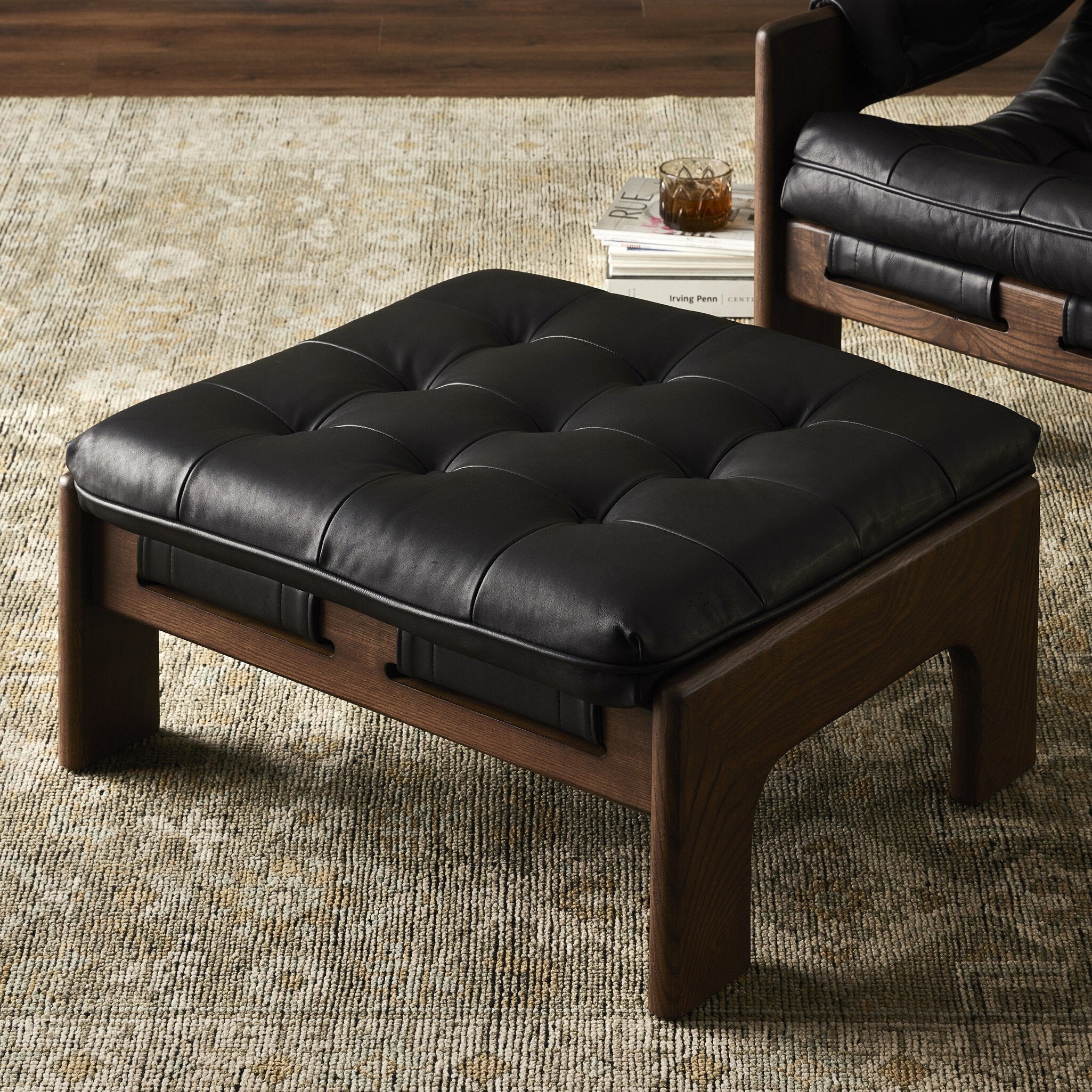 Black leather ottoman with wooden frame on a textured rug.