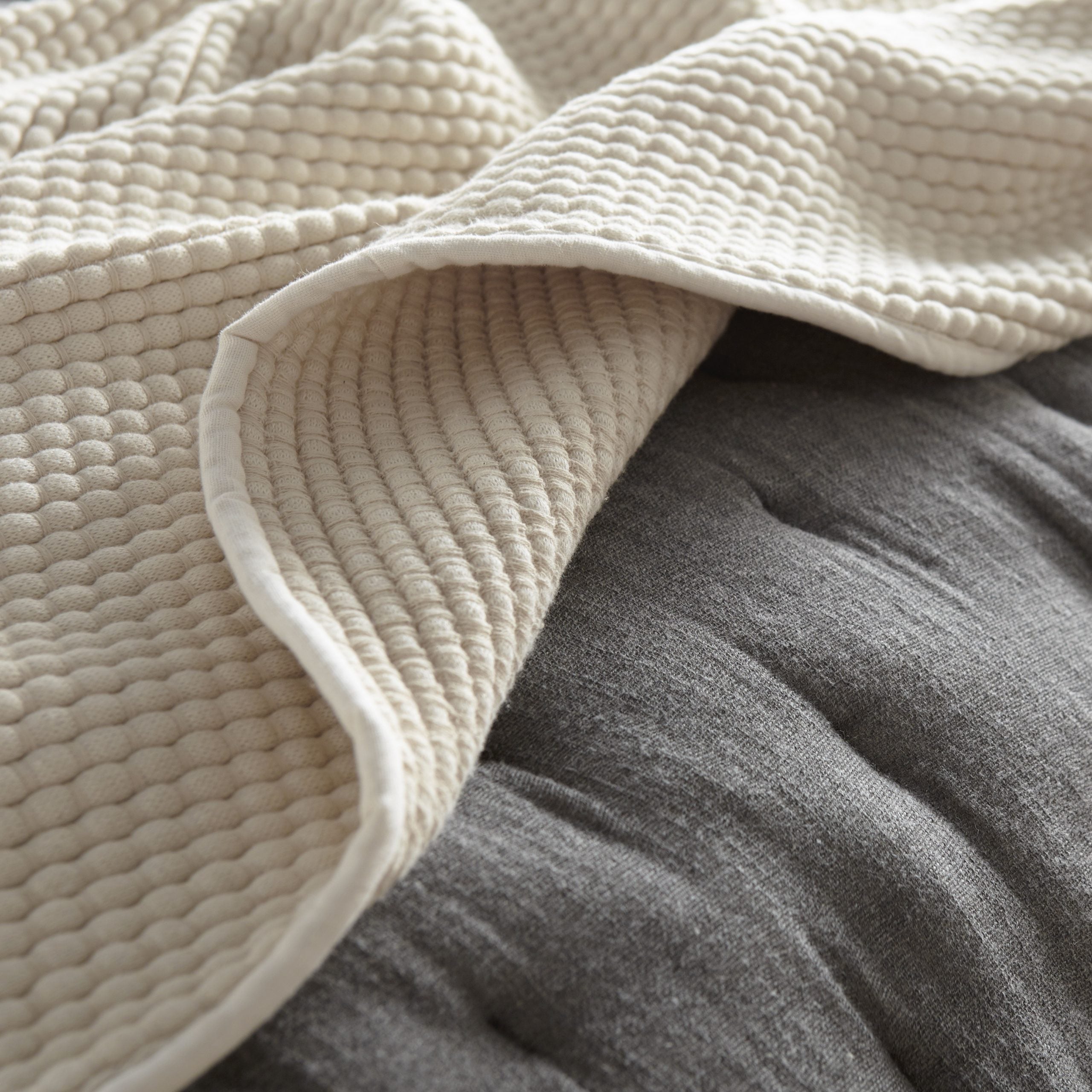 Ivory coverlet styled in natural light on a dark neutral background, showing fabric texture, material color, and relaxed drape.