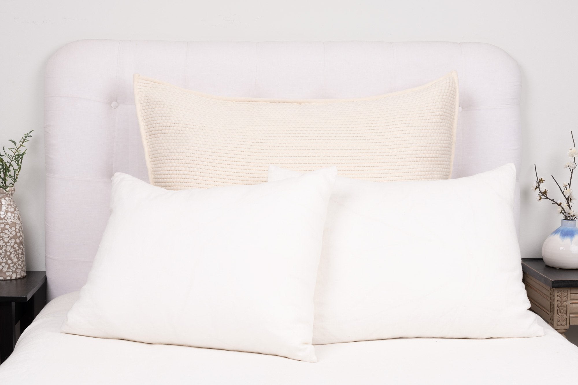 Large ivory pillow cover styled on a white bed showing knife edge or flange detailing, fabric texture, and muted palette.