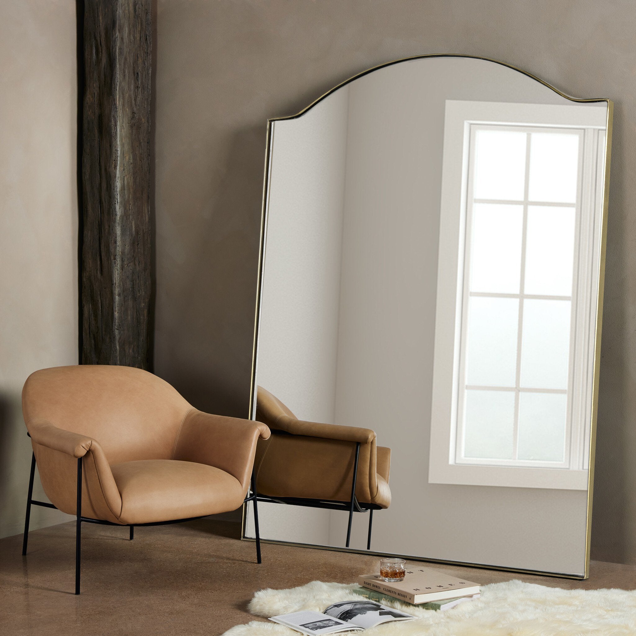 Beige armchair next to a large floor mirror in a room with a window.