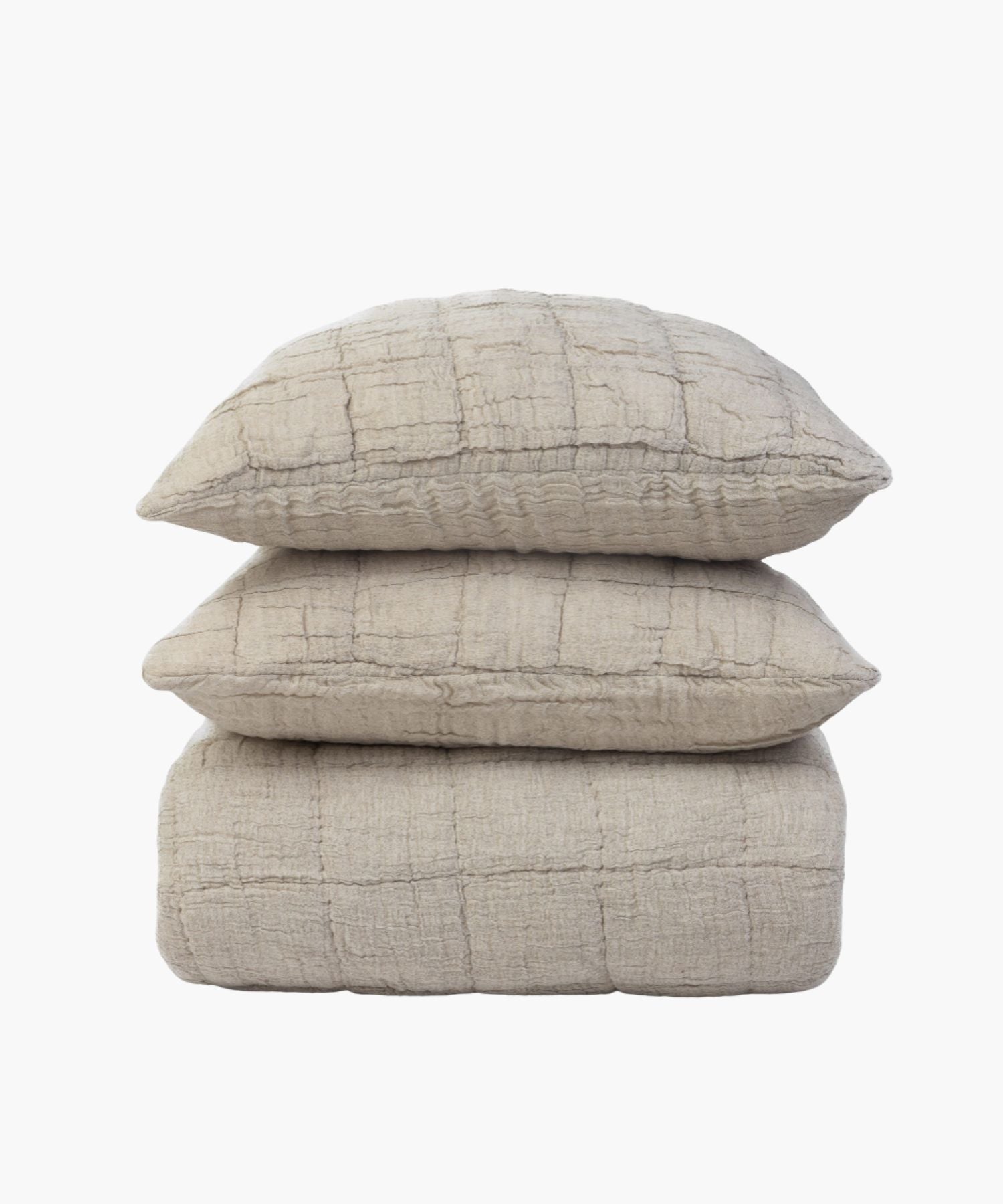 Beige cotton-linen quilt and matching shams stacked on top of eachother styled on a white background showing the material's subtle puckering and soft stitching.