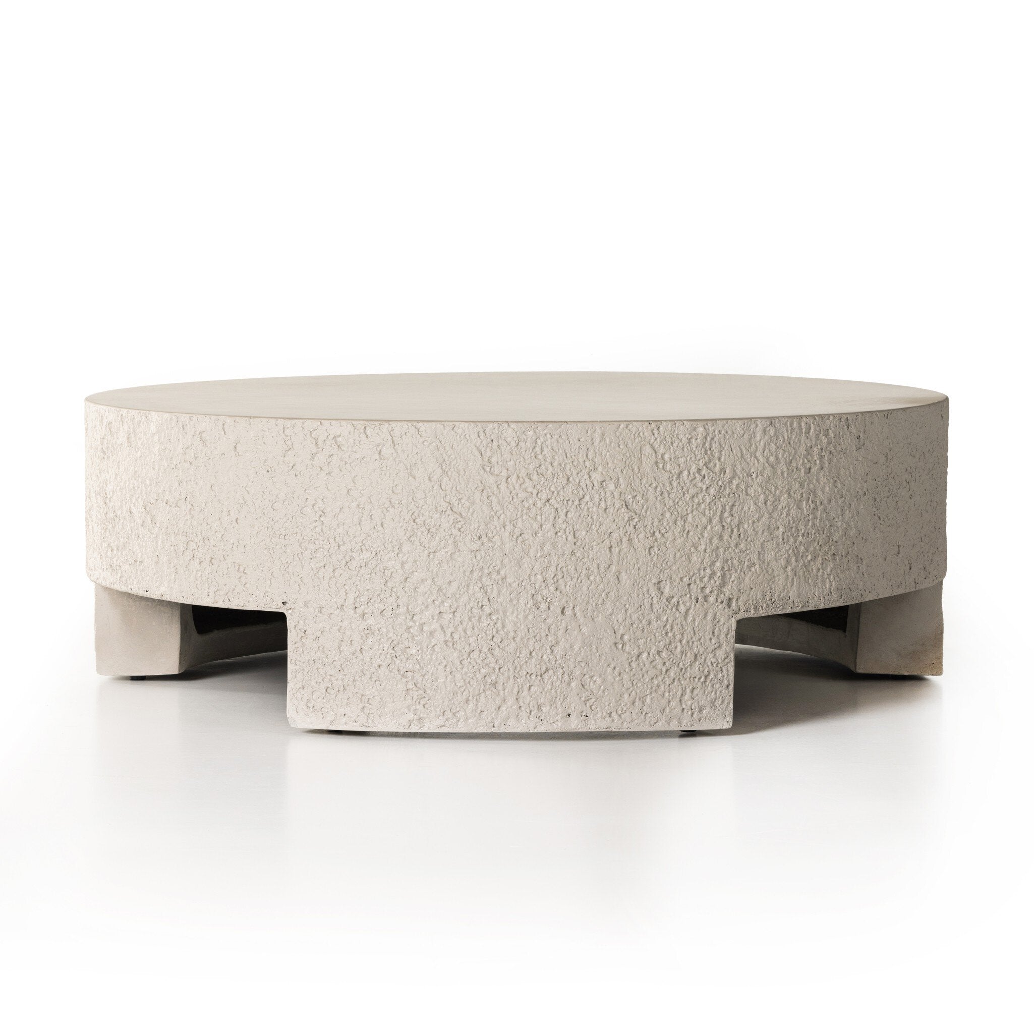A round pumice concrete coffee table with a smooth top and cutout legs.