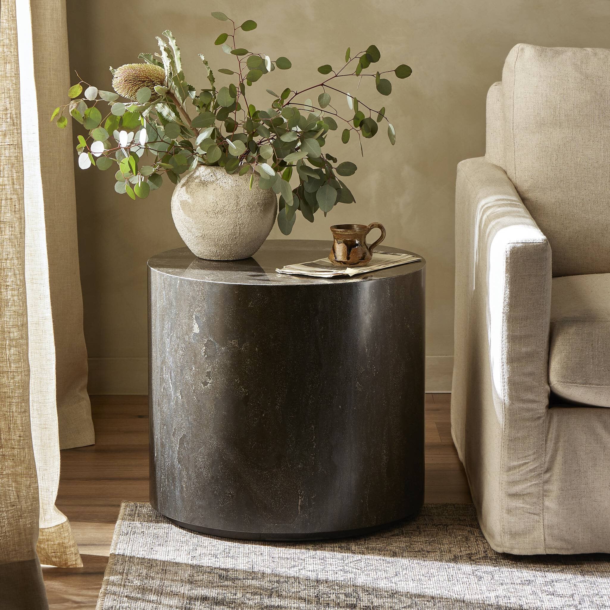 Round dark stone table with a vase of greenery and a mug in a living room setting.