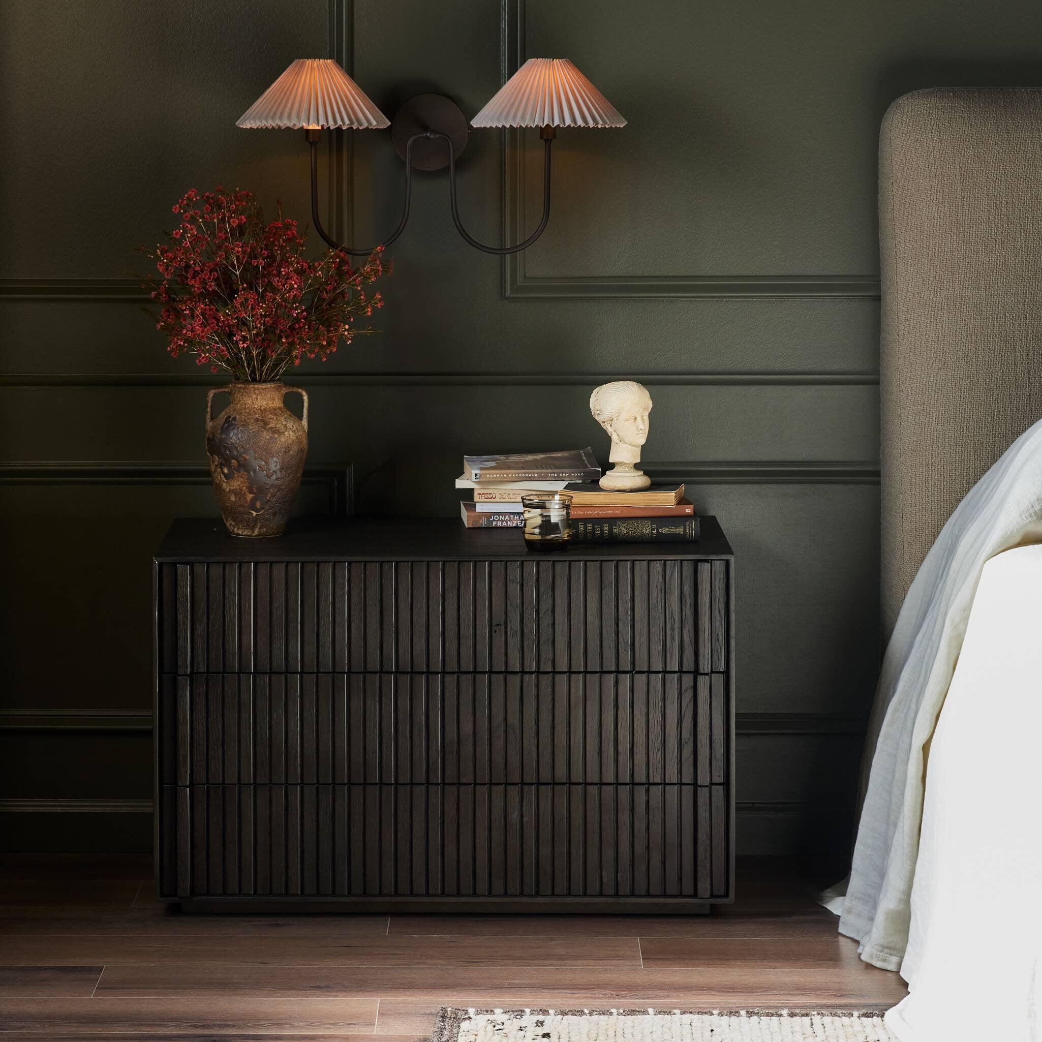 Dark wooden nightstand with decorative items against a dark wall