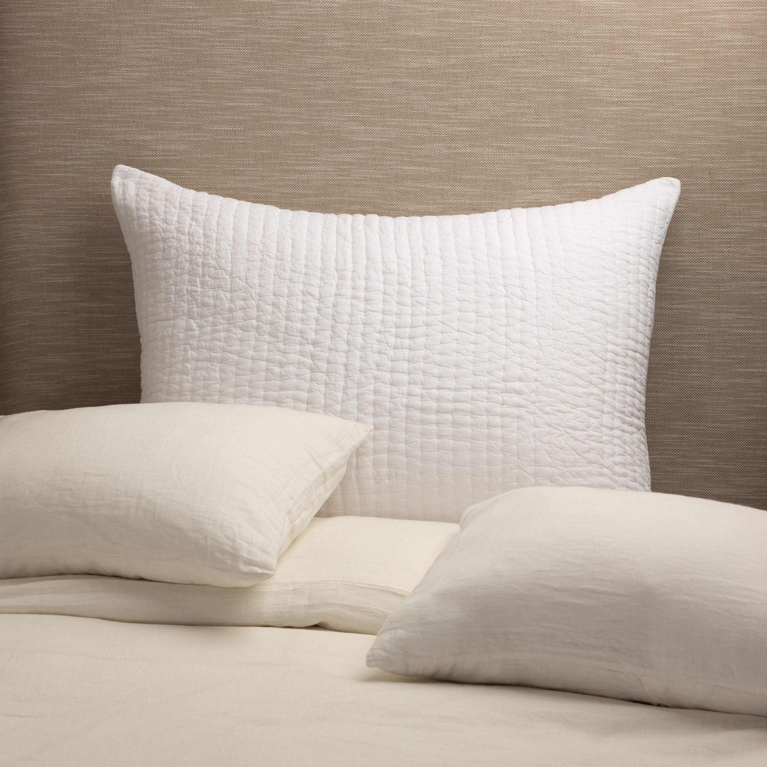 Maegan Sham styled against a neutral headboard with cream linen bedding, showcasing its texture and casual elegance.