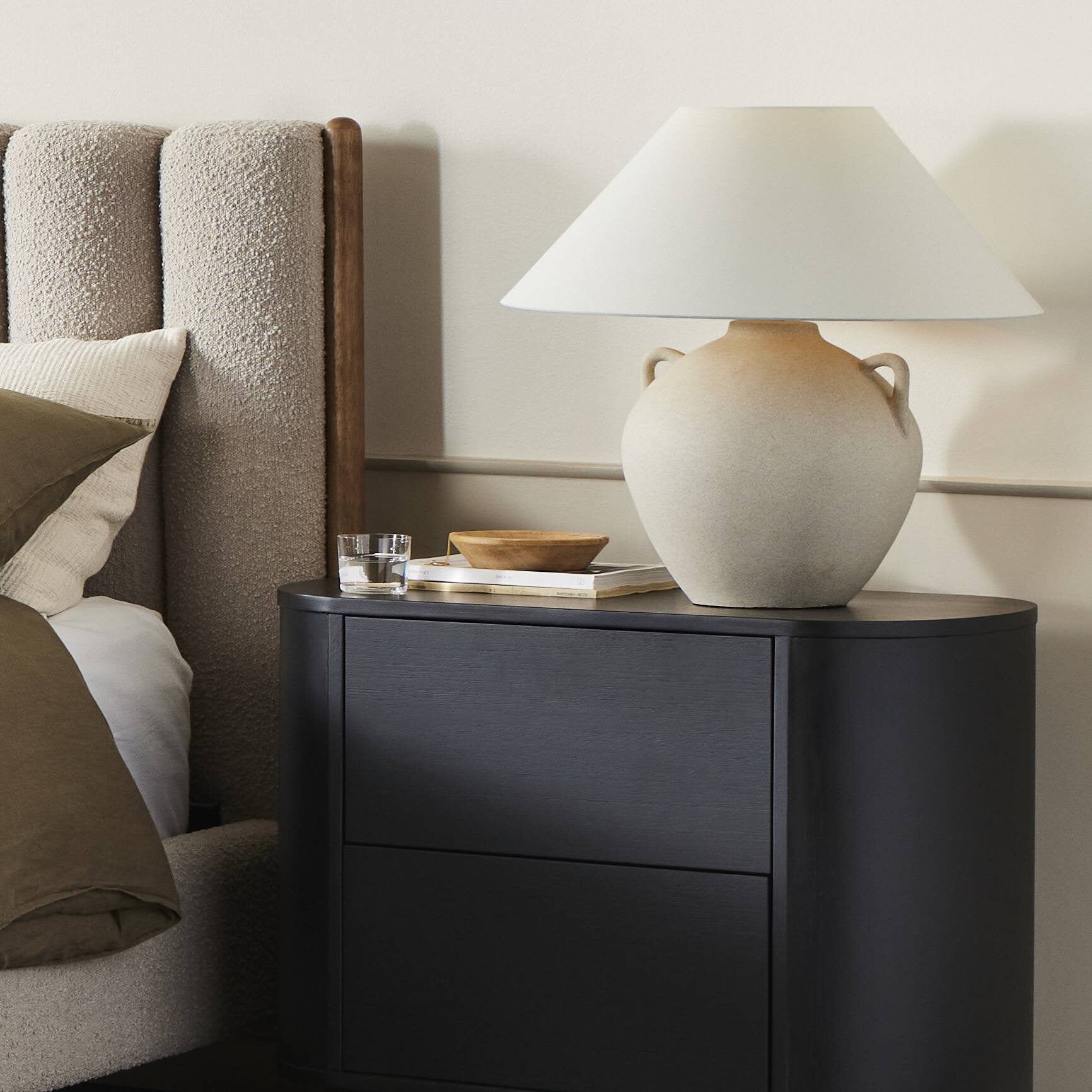 Black nightstand with a lamp and decorative items next to a bed.
