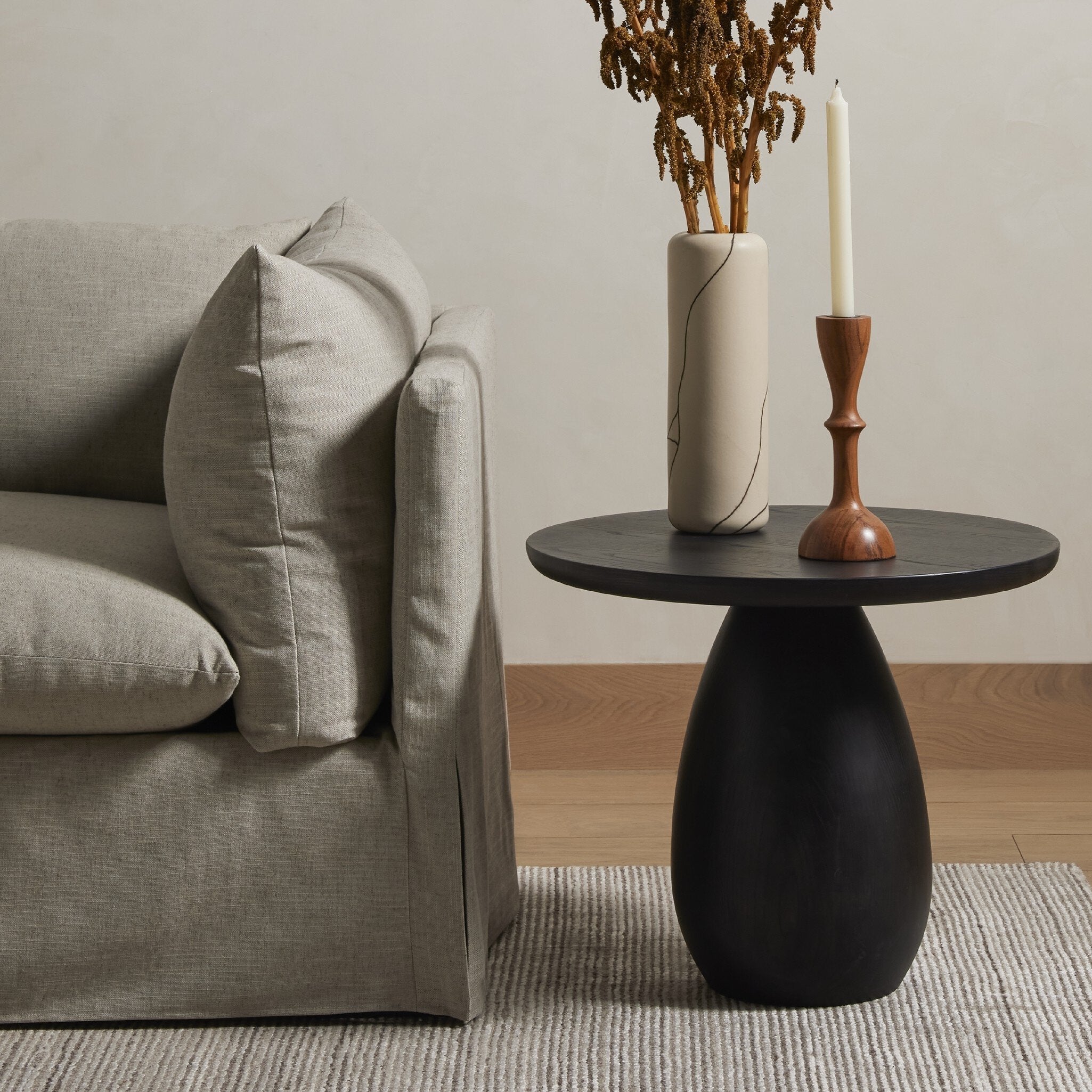 Black side table with a candle and vase next to a gray sofa in a living room.