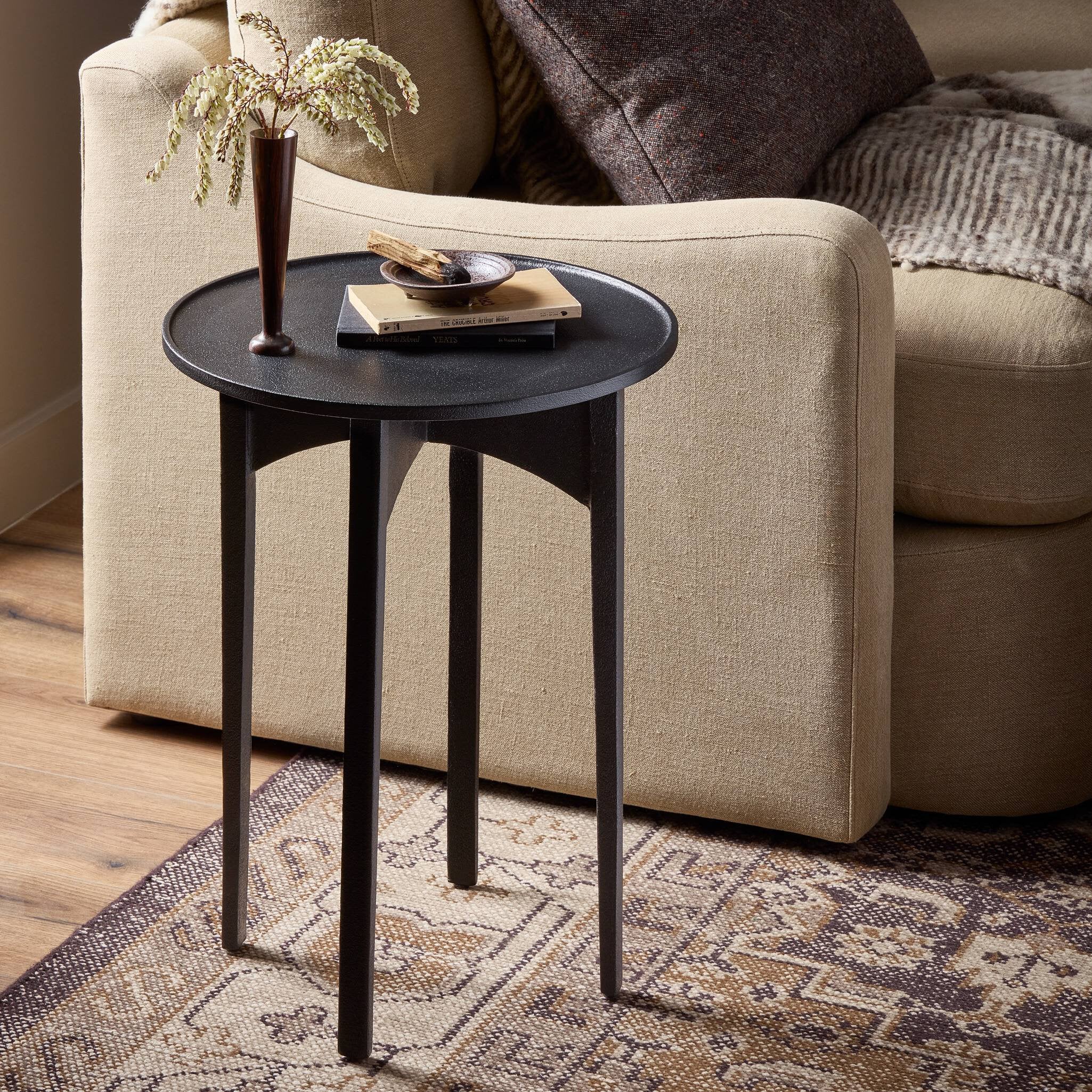 Small black side table with decorative items in front of a beige sofa.