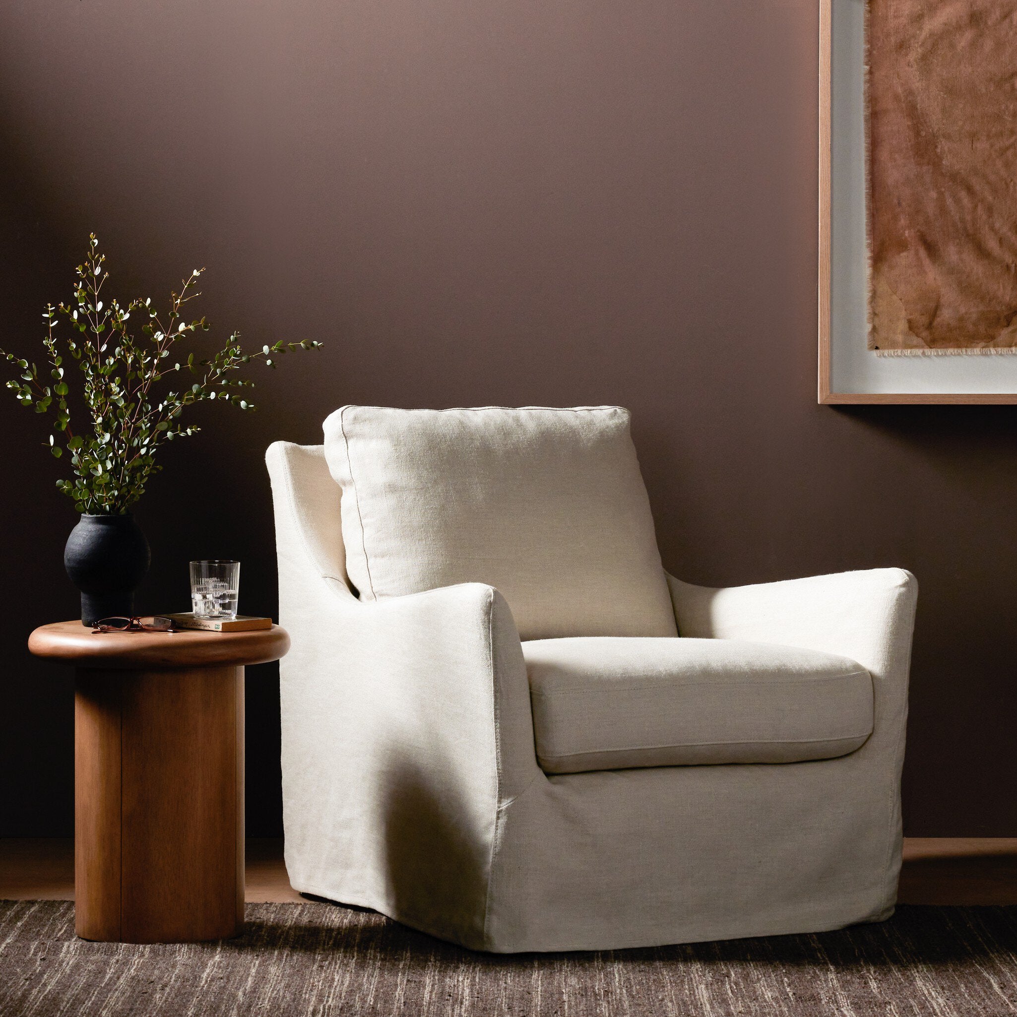 Ivory armchair in a room with a wooden side table and plant against a brown wall.