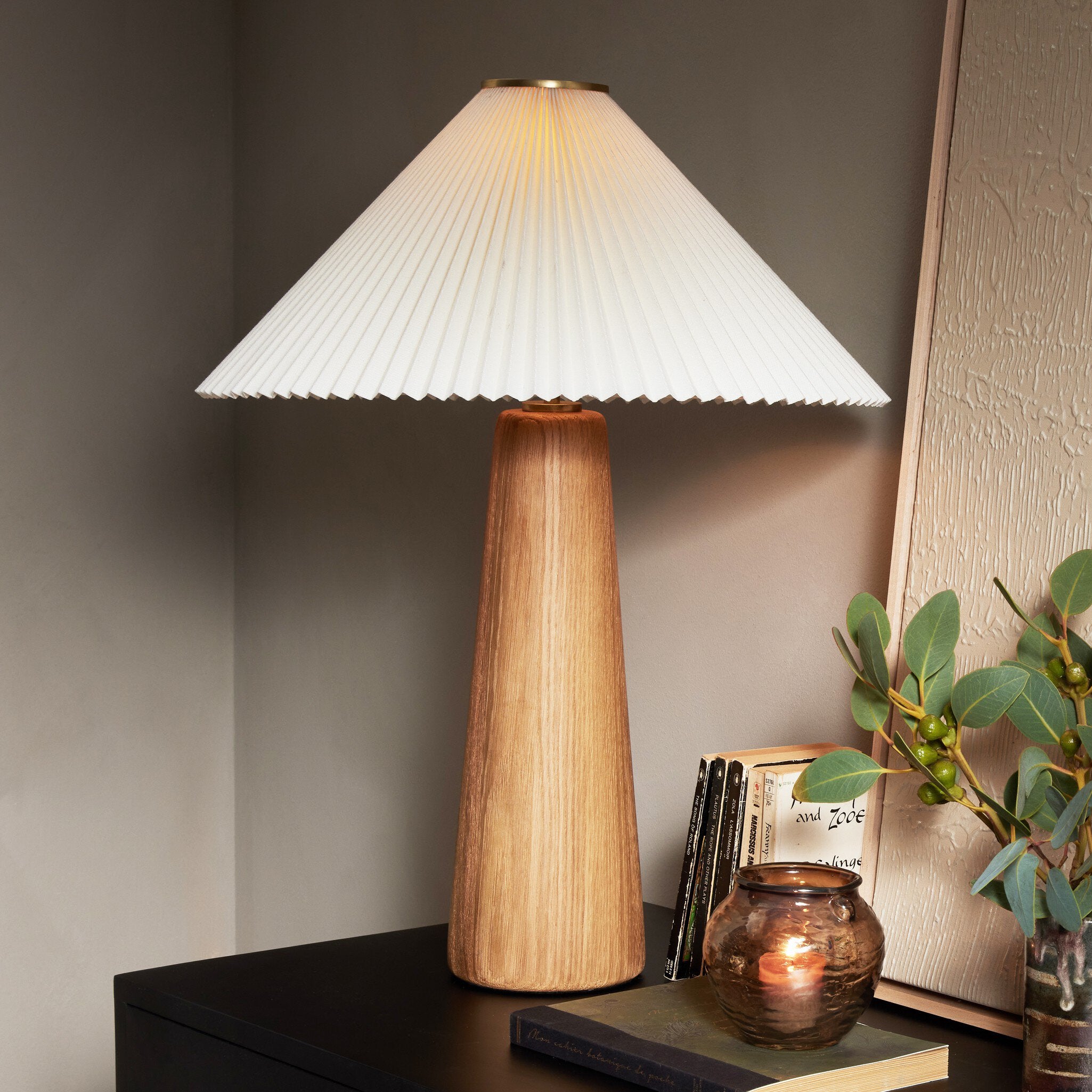 Wooden table lamp with pleated white shade on a dark surface.