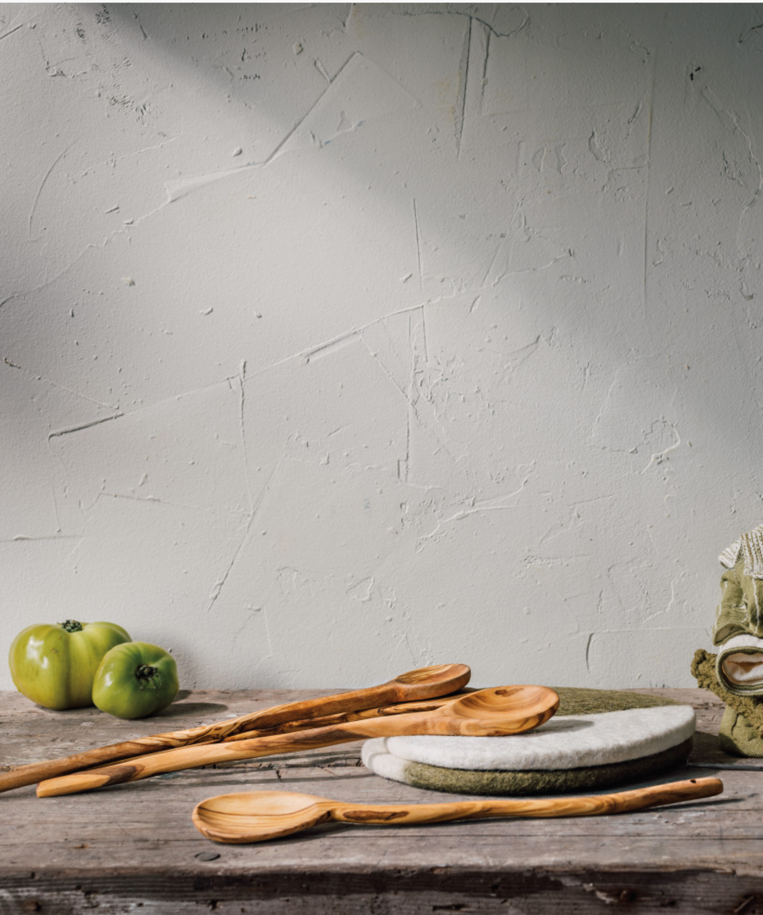 A wooden spoon with a smooth, elongated handle and a round head, featuring natural light and dark brown grain patterns styled with other wood spoons and a rustic table.