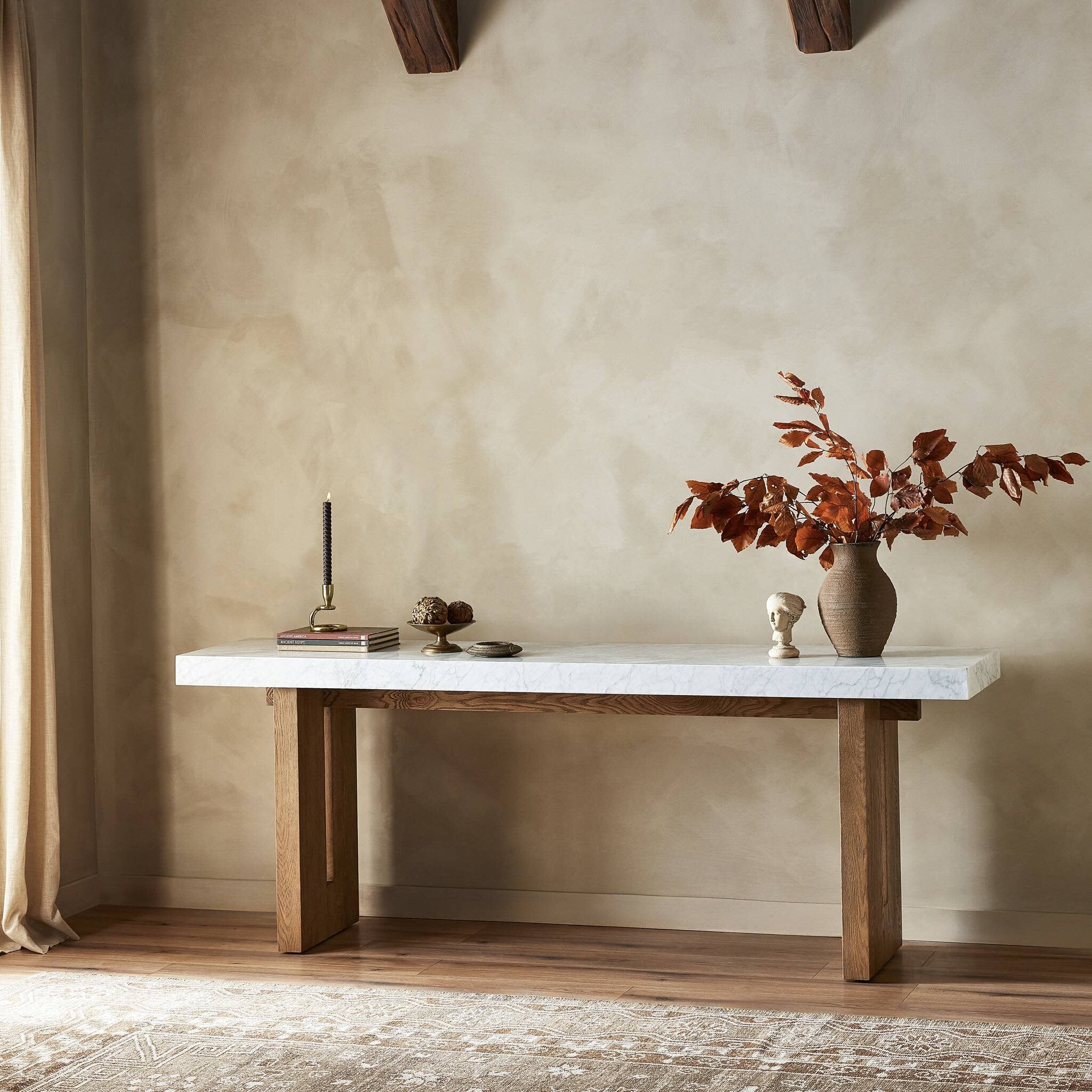 Wooden table with marble top against a beige wall, featuring decorative items.