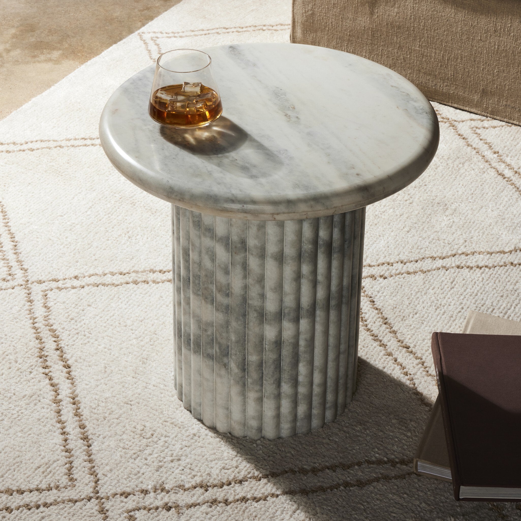 Marble end table with a glass of whiskey on a patterned rug.