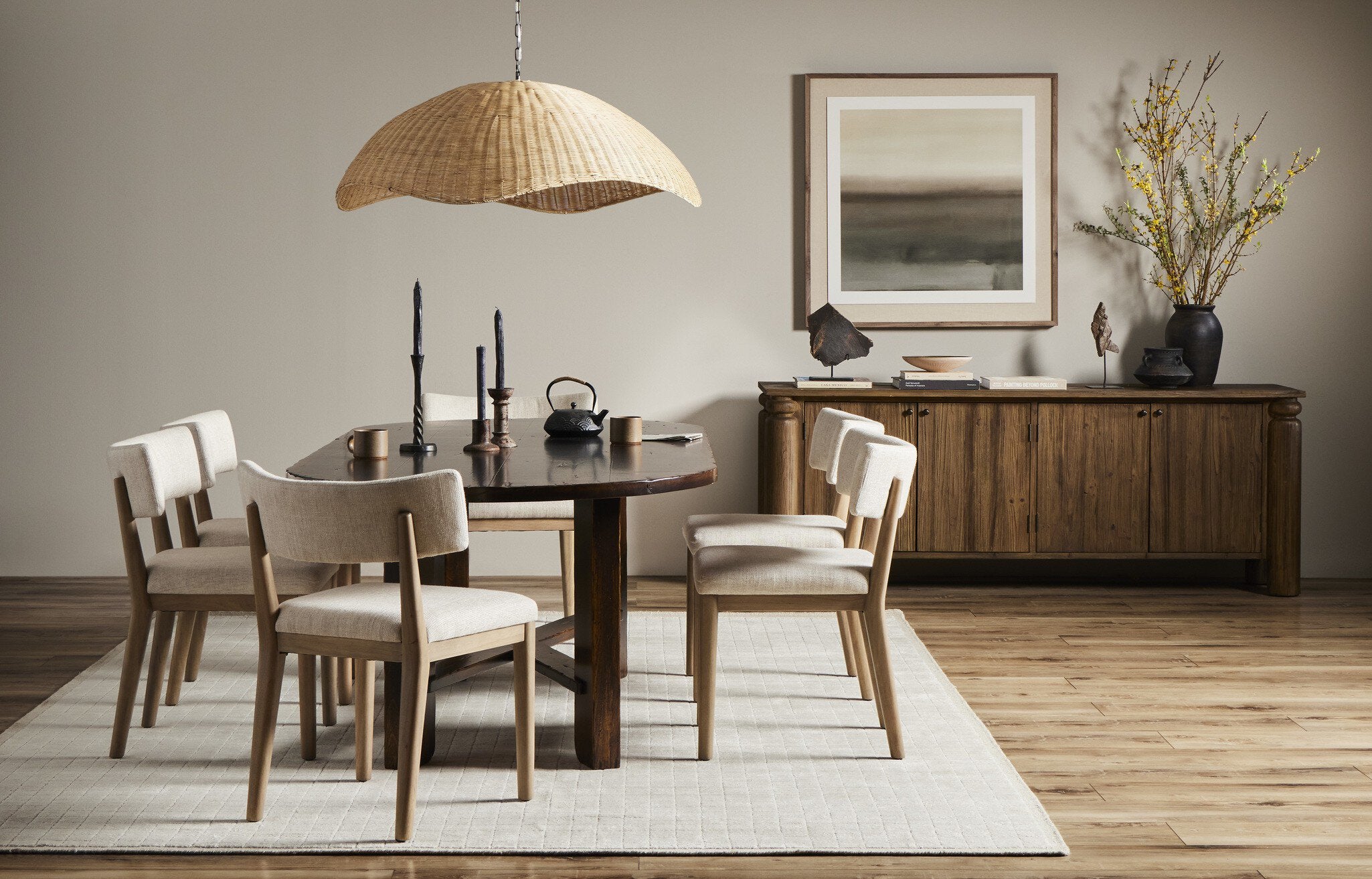 Dining room with wooden table and chairs, wicker pendant light, and abstract painting.
