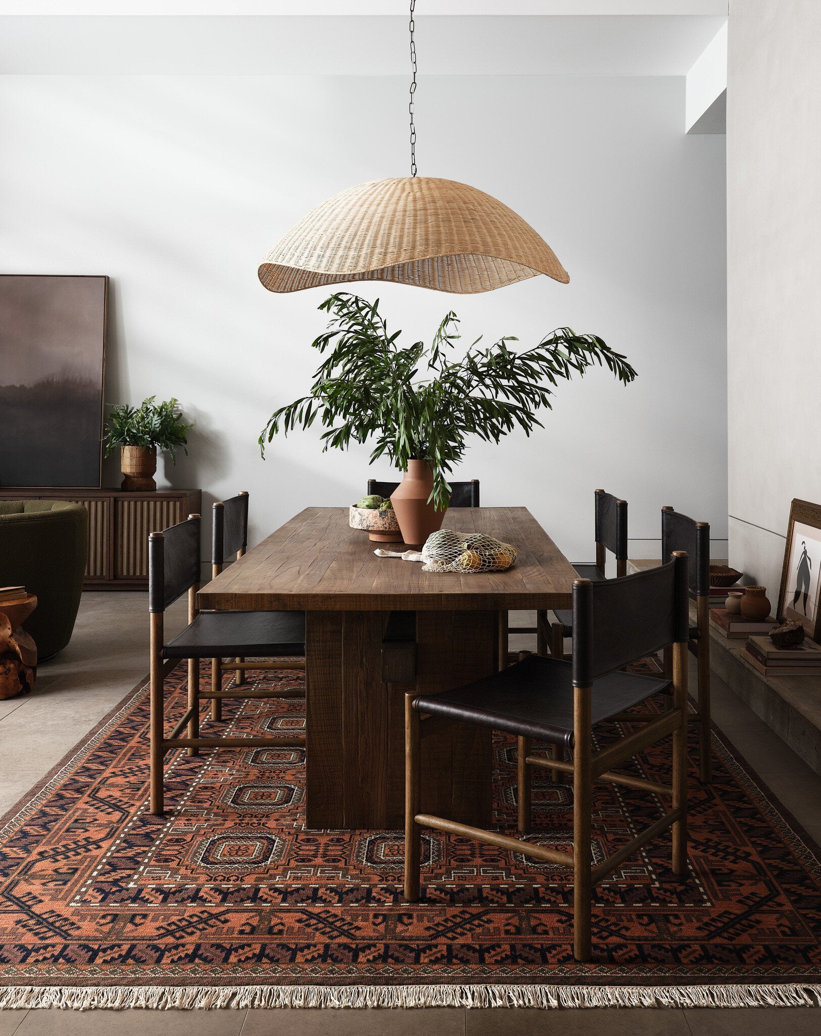 Dining room with wooden table, chairs, and a wicker pendant light.