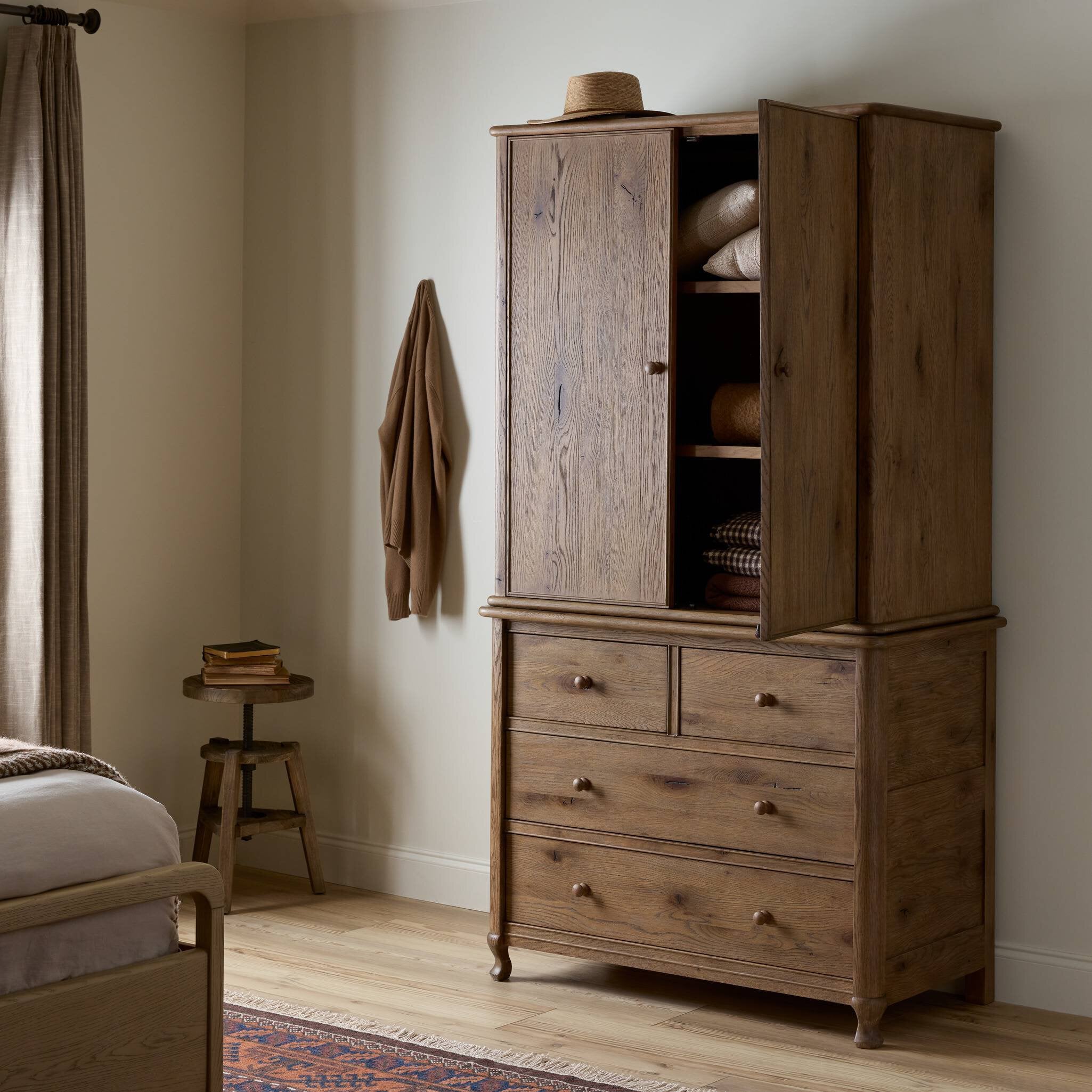Wooden armoire with open doors in a bedroom setting.