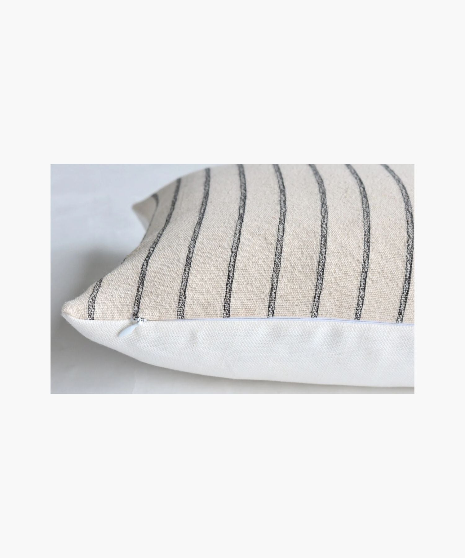 A close up picture of a pillow cover with vertical black woven stripes on a cream background. The pattern is simple and elegant, conveying a calm and cozy atmosphere.