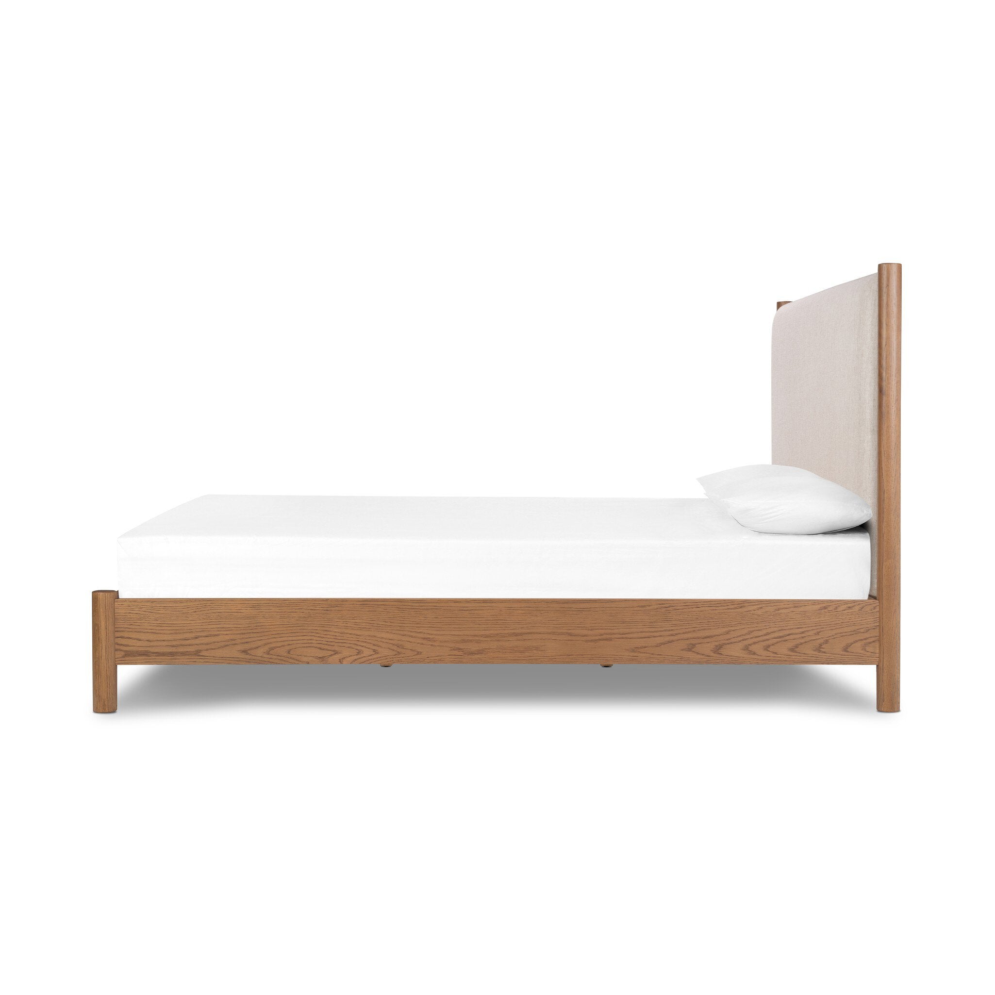 Side profile of a wooden bed with upholstered headboard and white bedding on a white background.