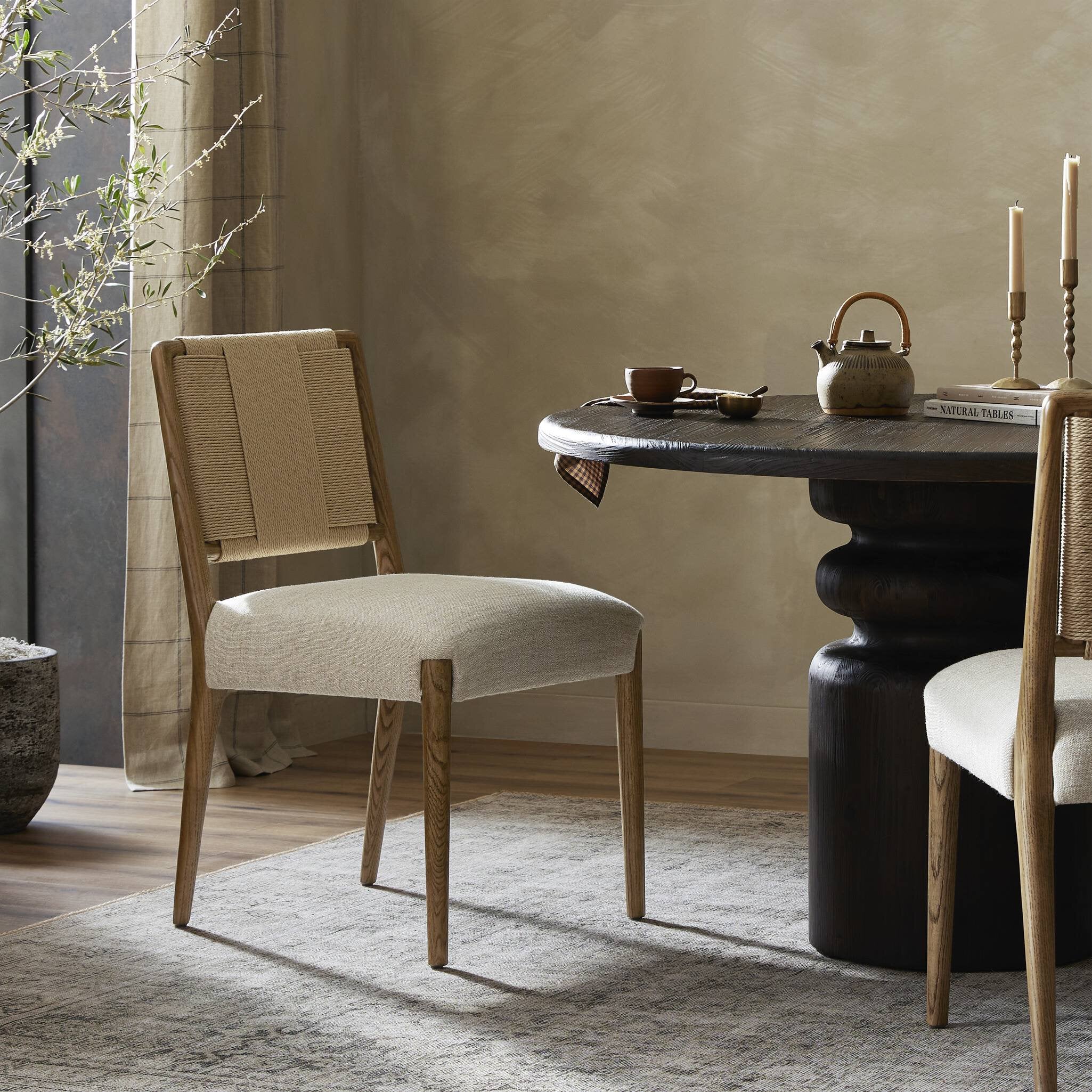Dining room with a black round table and wooden chairs against a beige wall.
