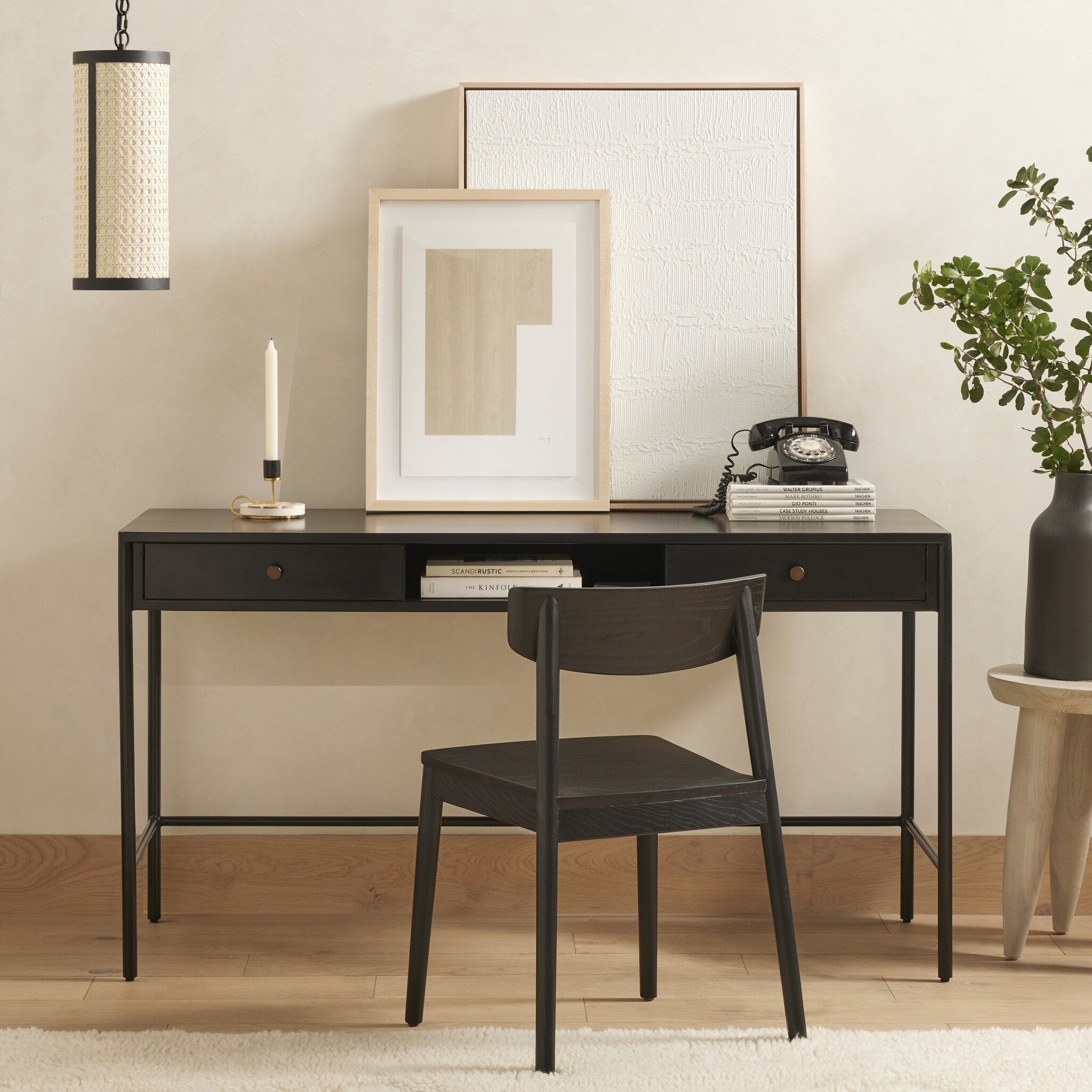 Black desk with chair, framed art, and decorative items in a room.