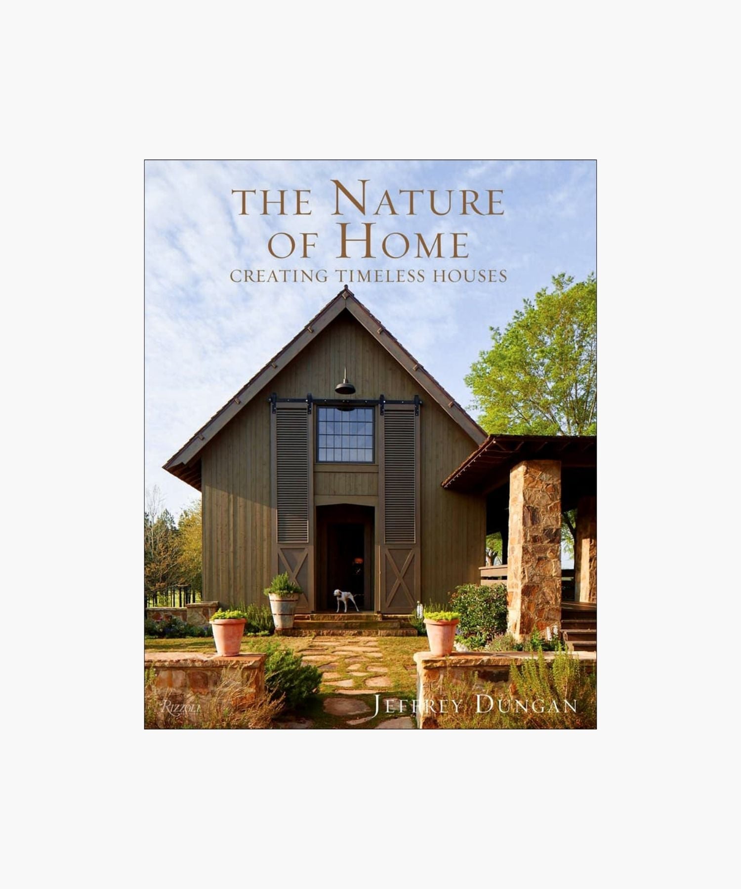 The cover of the book "The Nature of Home" by Jeffrey Dungan, featuring a rustic house with wooden siding, large windows, stone pillars, and surrounding greenery under a clear sky.