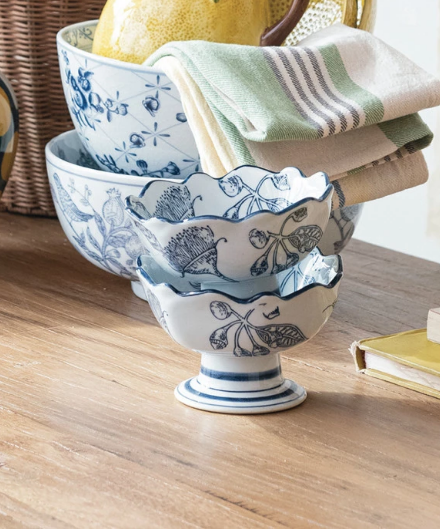Two Elegant bowls with a wavy rim, decorated with intricate blue floral designs stacked together and styled with kitchen accessories.