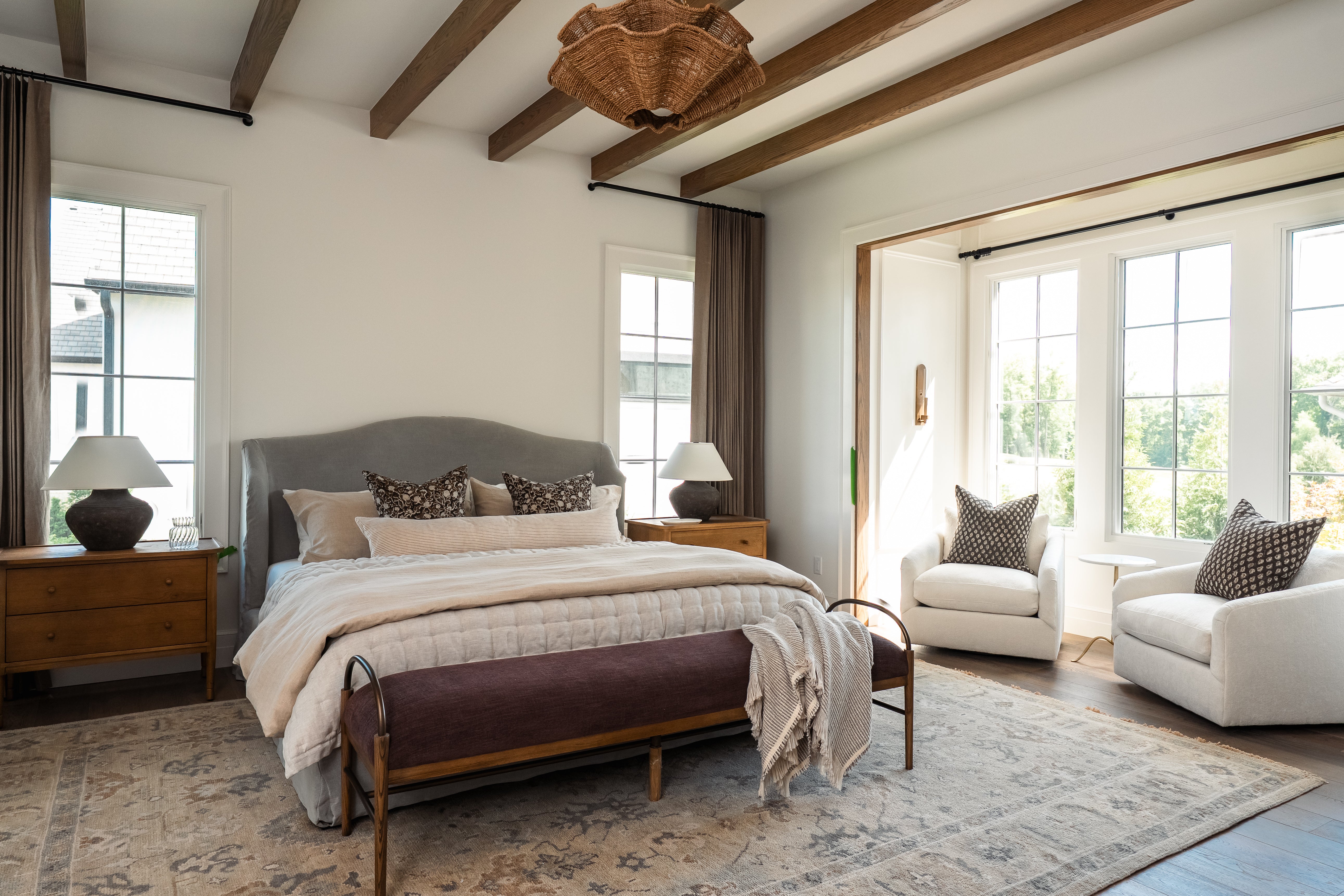 Modern bedroom with a bed, chairs, and large windows.