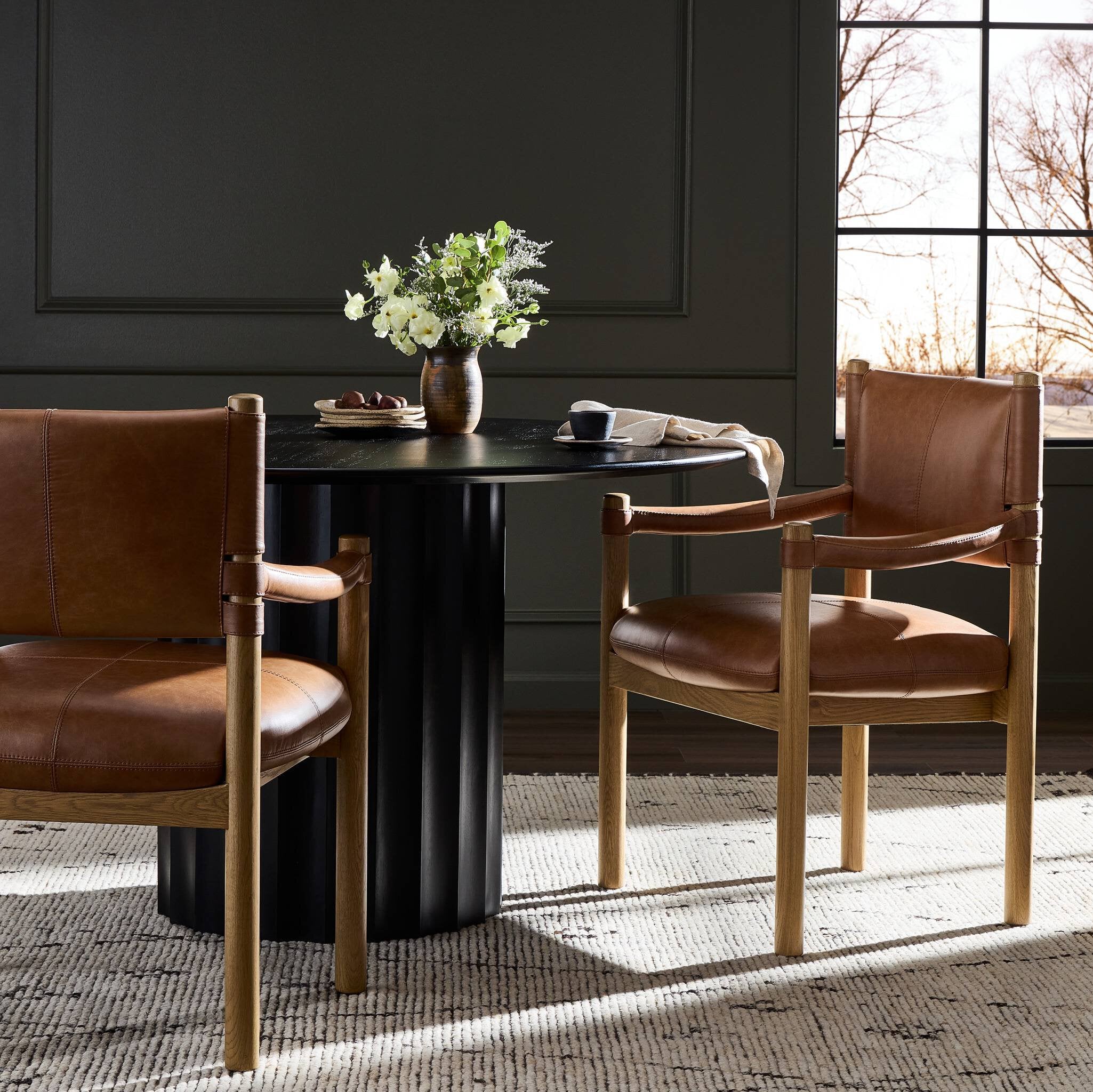 Dining area with black round table and brown leather chairs against a dark wall.