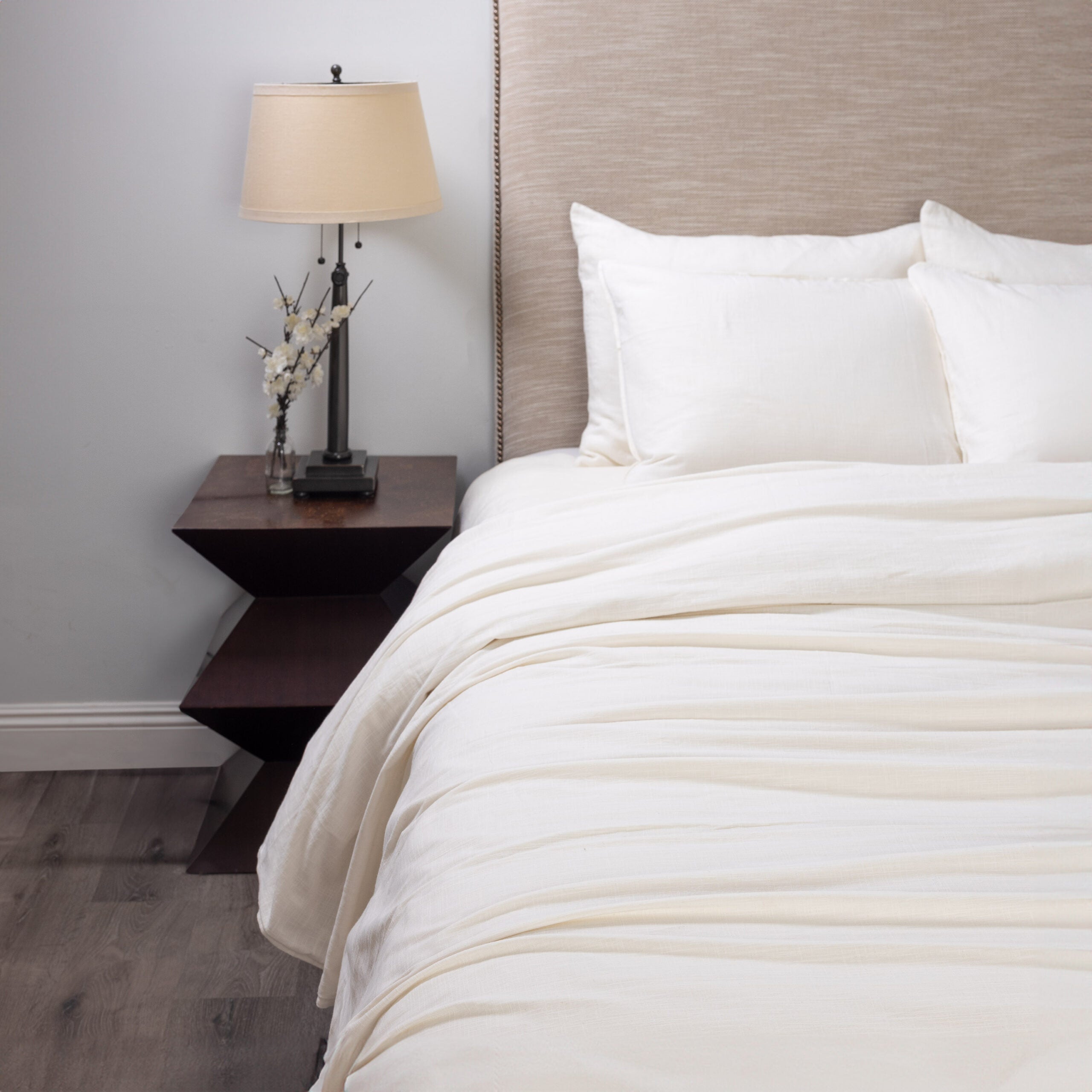 Neatly made bed with neutral linen bedding in a bedroom setting.
